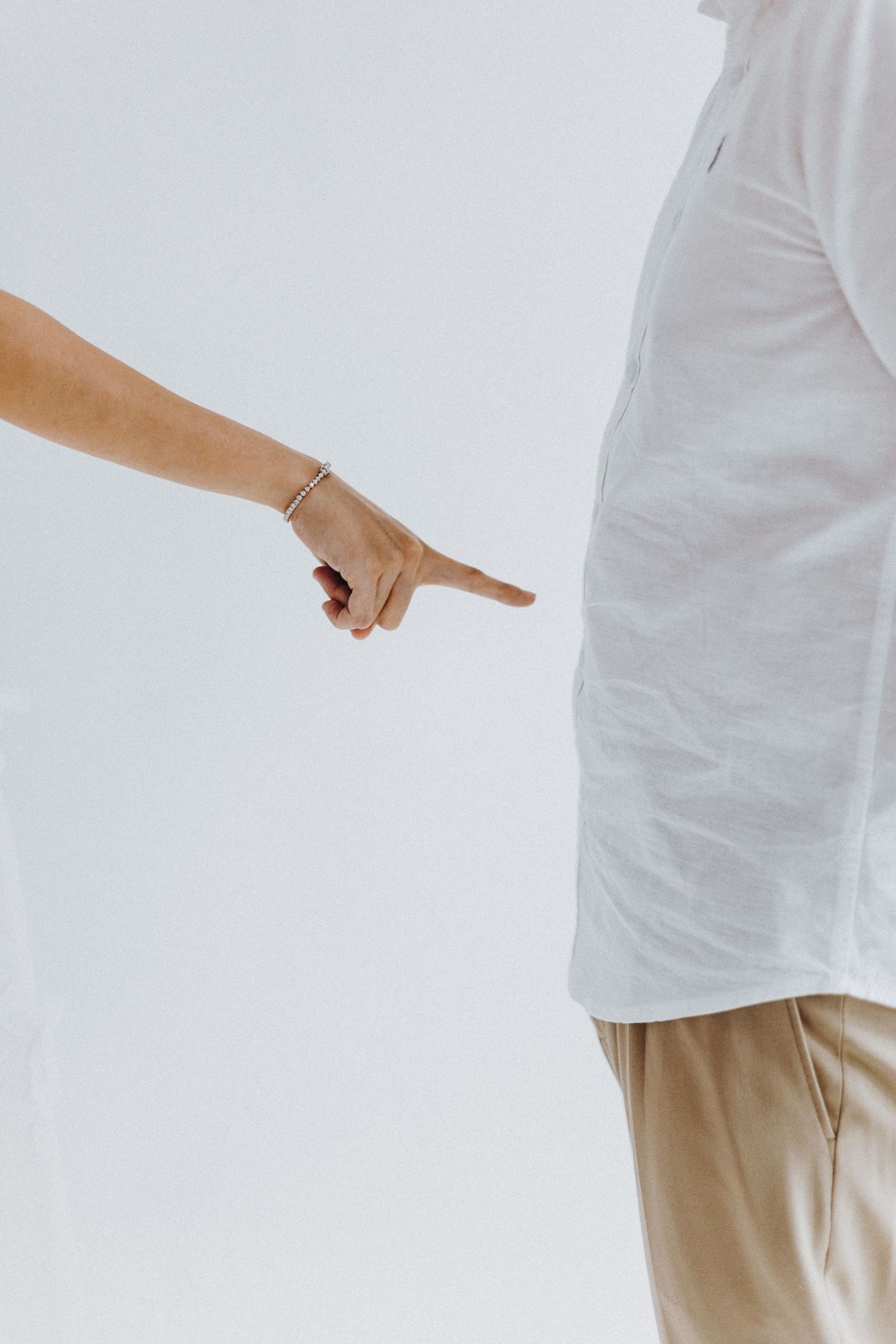 A finger points accusingly at someone wearing white clothing against a light background.