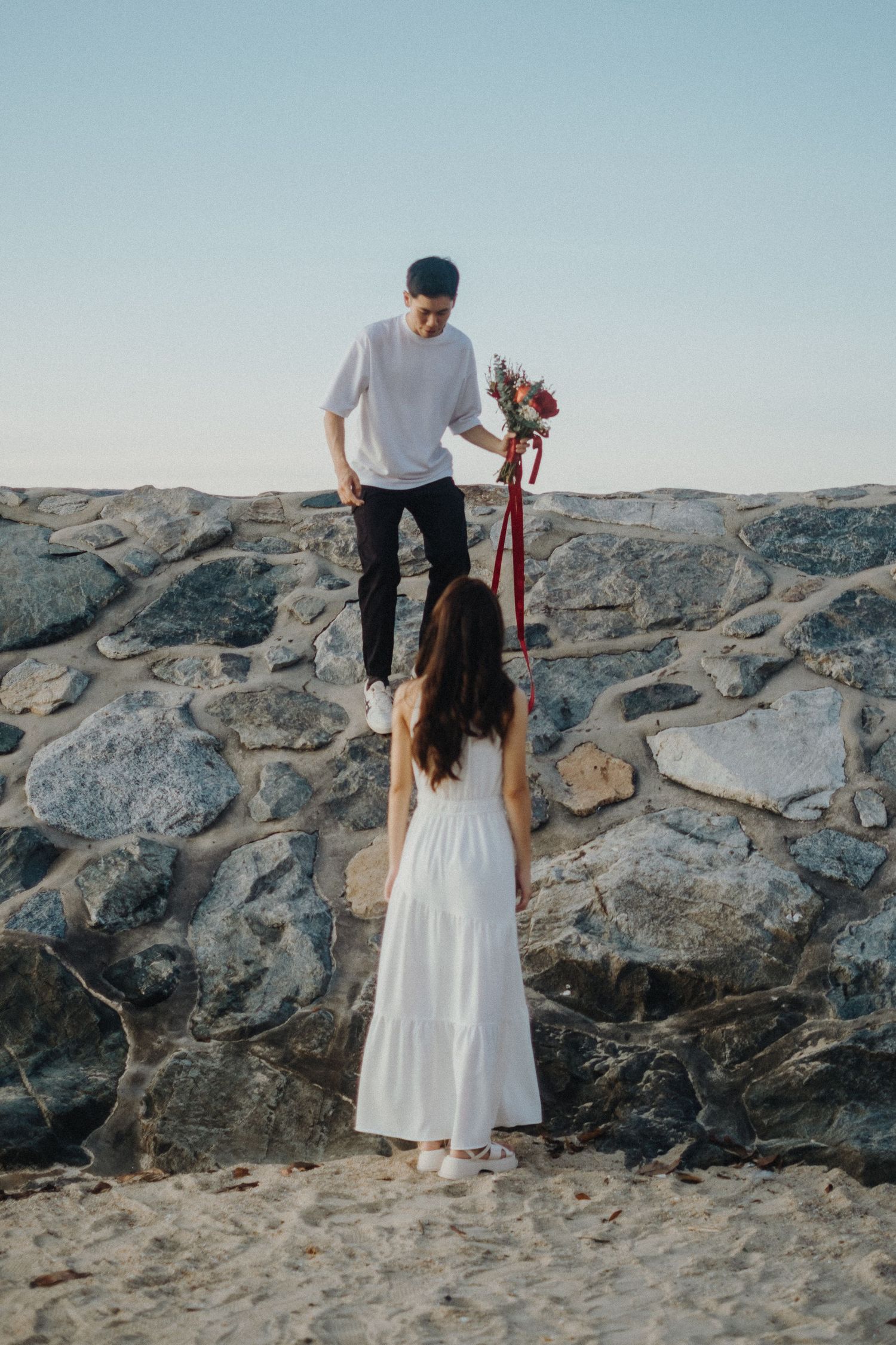 Couple on rocky beach sharing romantic moment with flowers.