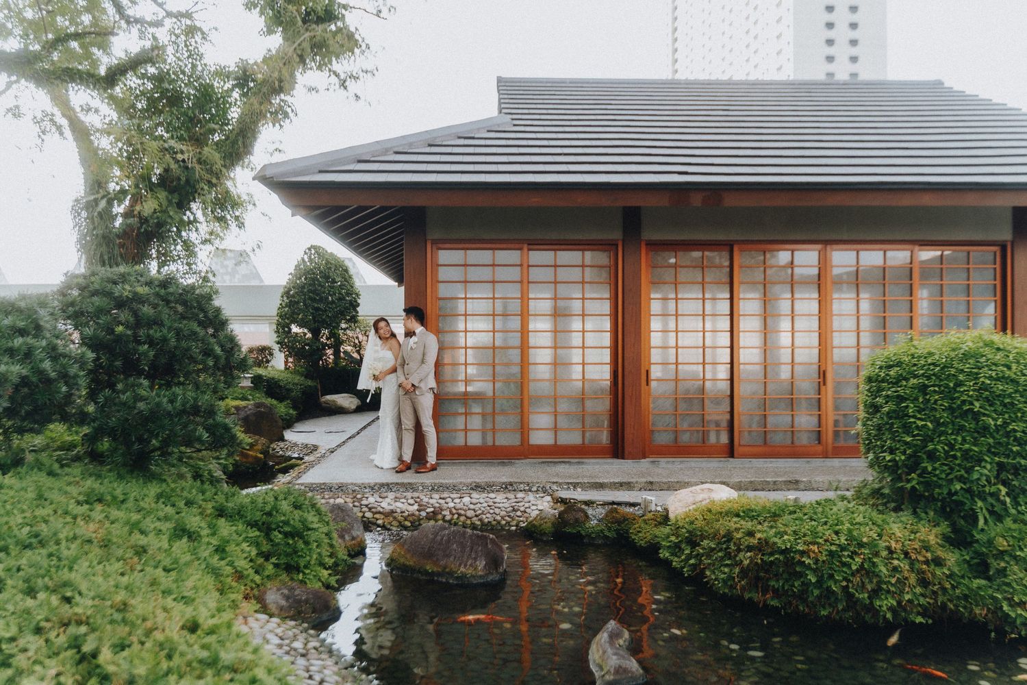 Traditional Japanese garden house with sliding doors and koi pond surrounded by lush greenery and landscaping.