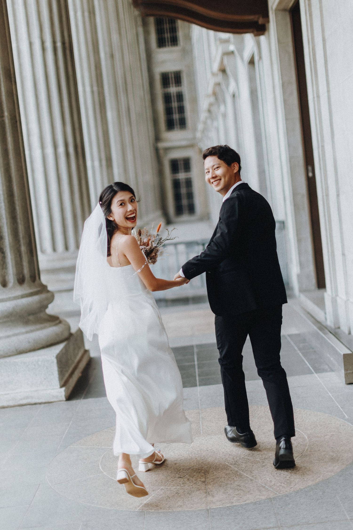 A couple in formal attire dances and laughs between classic white columns.