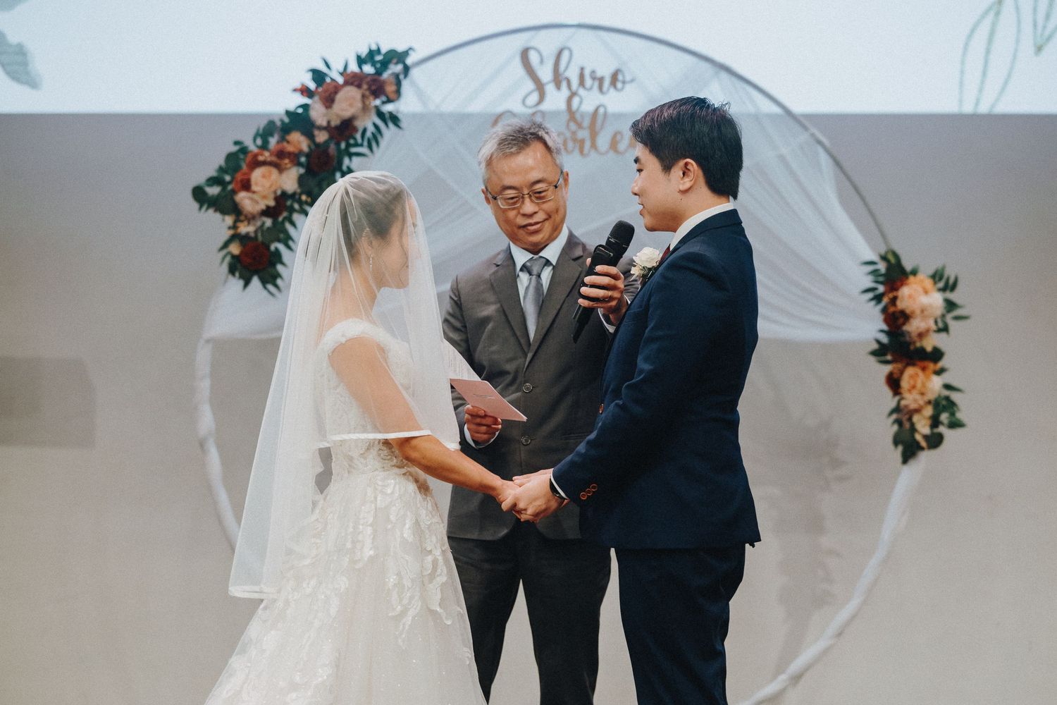 Wedding ceremony under white arch decorated with pink and peach floral arrangements.