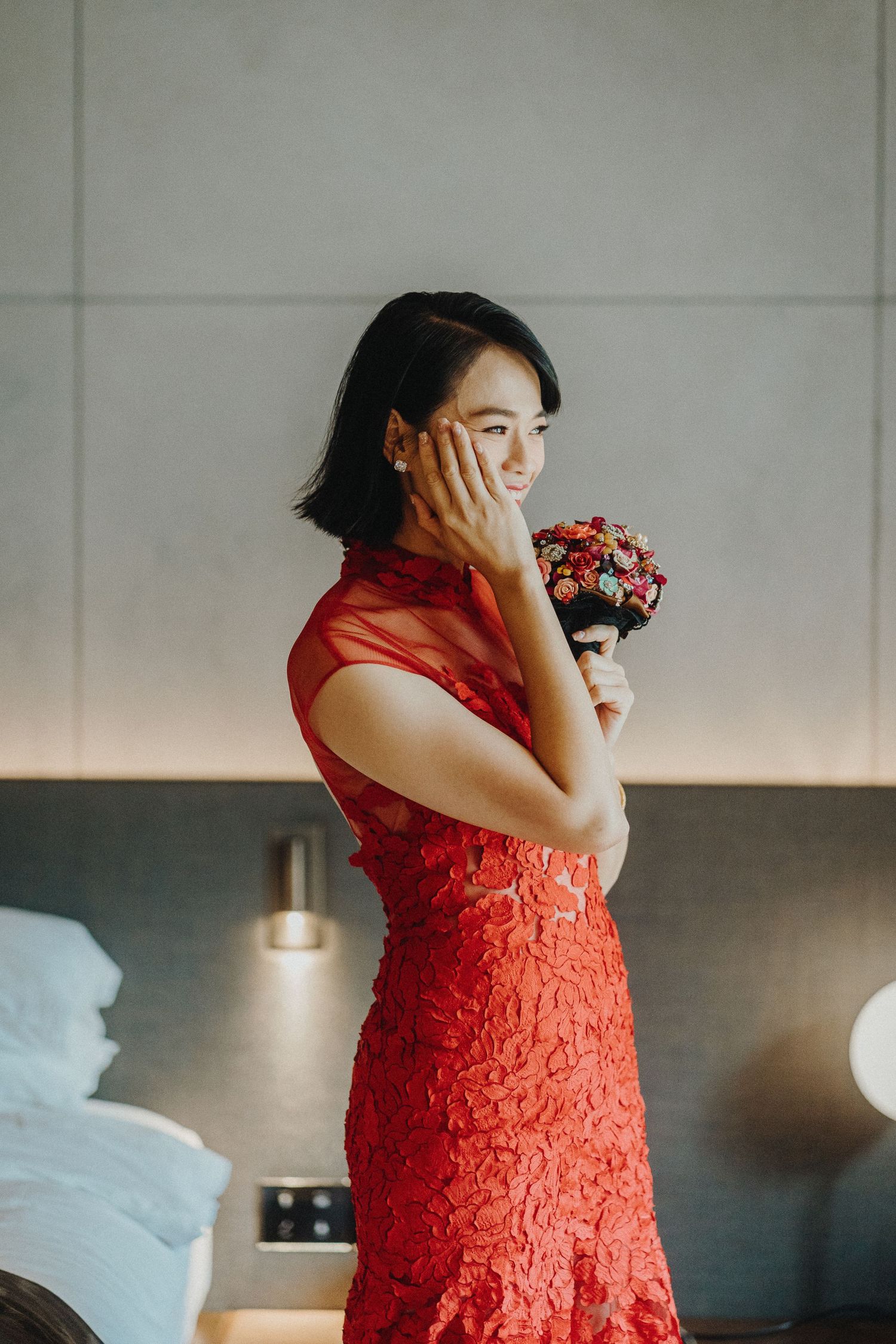 Woman wearing a vibrant red lace dress during an emotional moment in what appears to be a getting-ready scene.