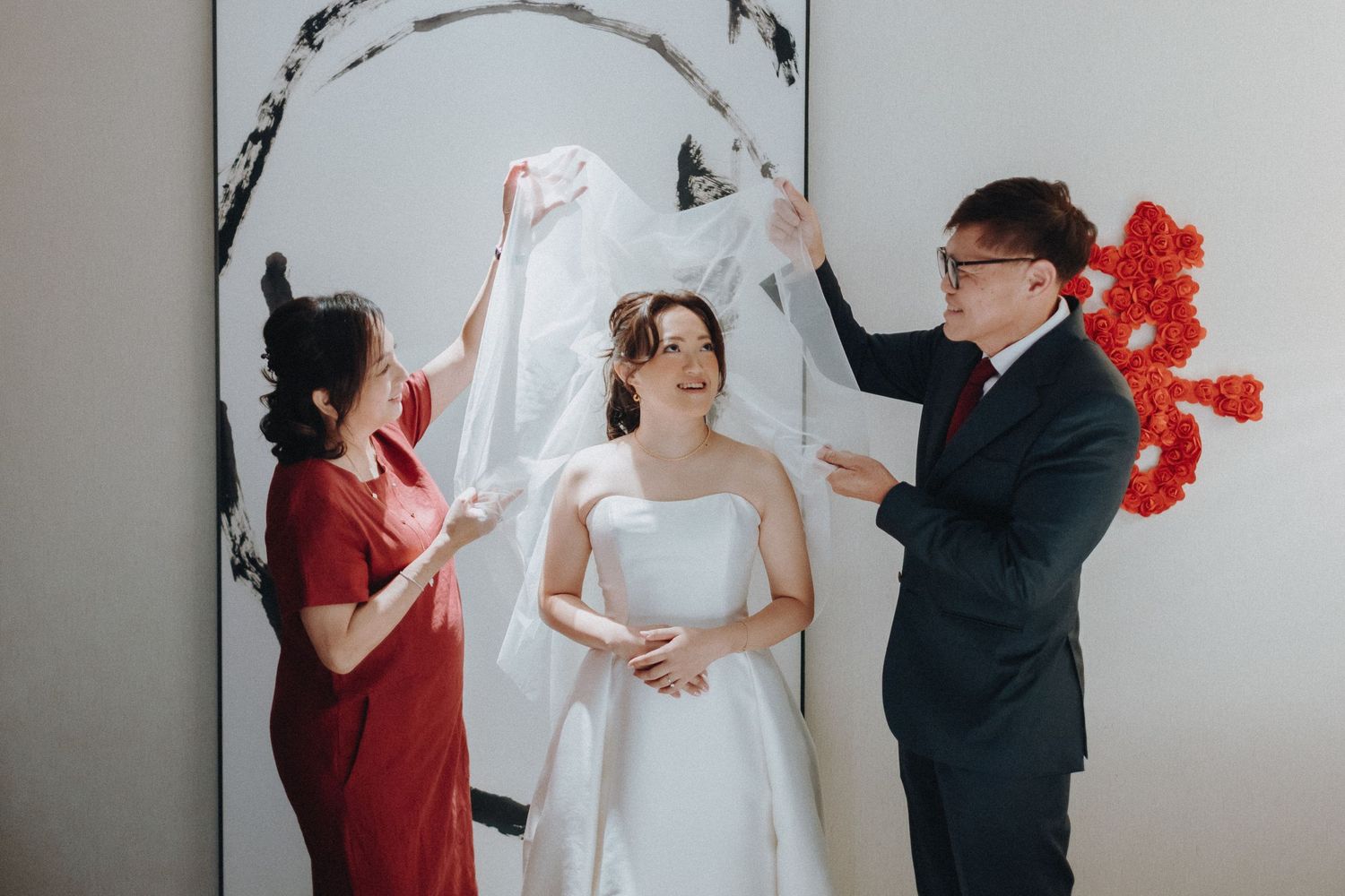 Wedding party interacts playfully during photo session with red floral wall decor.