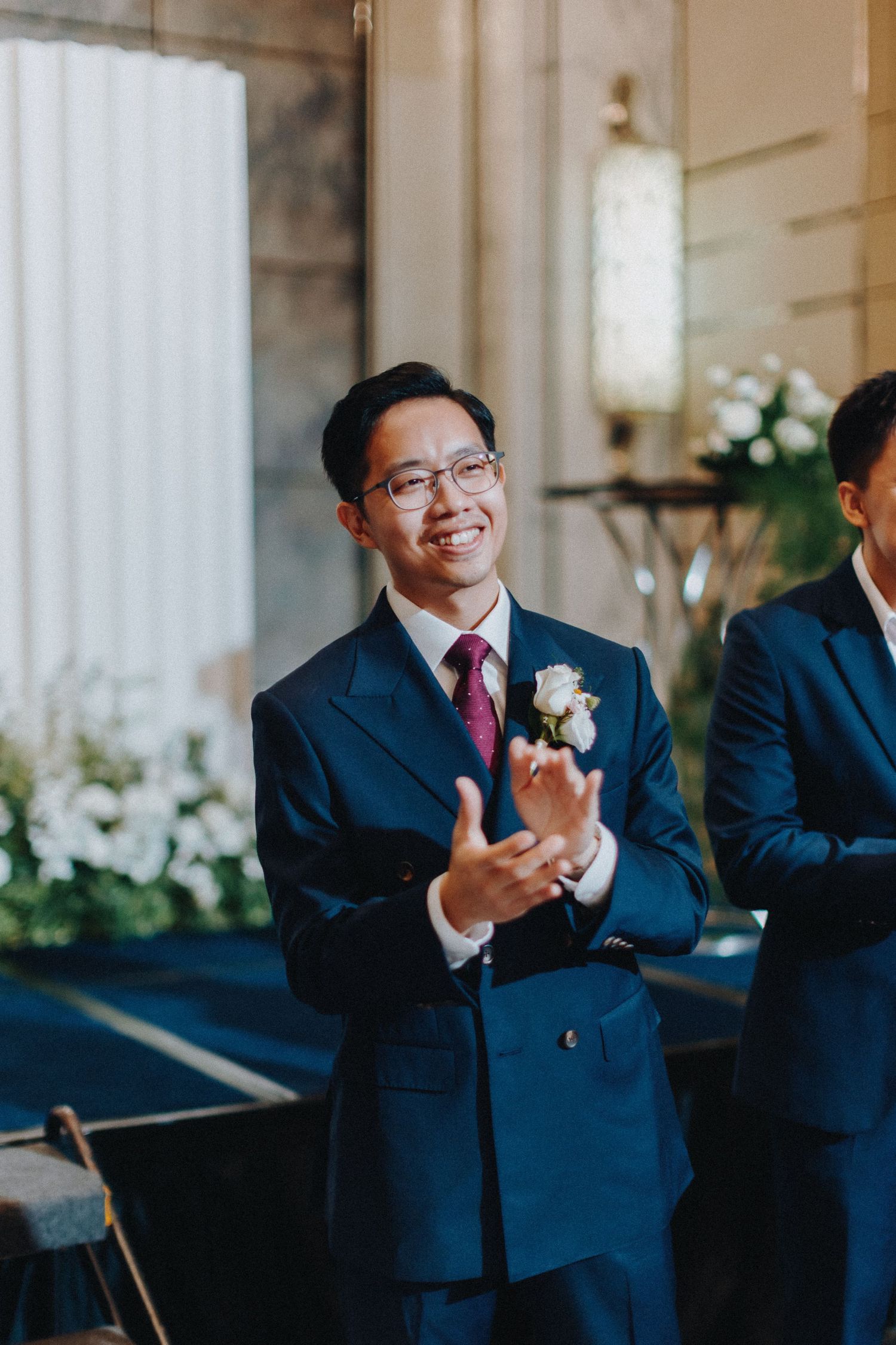 Wedding guests in navy suits applaud during the ceremony.