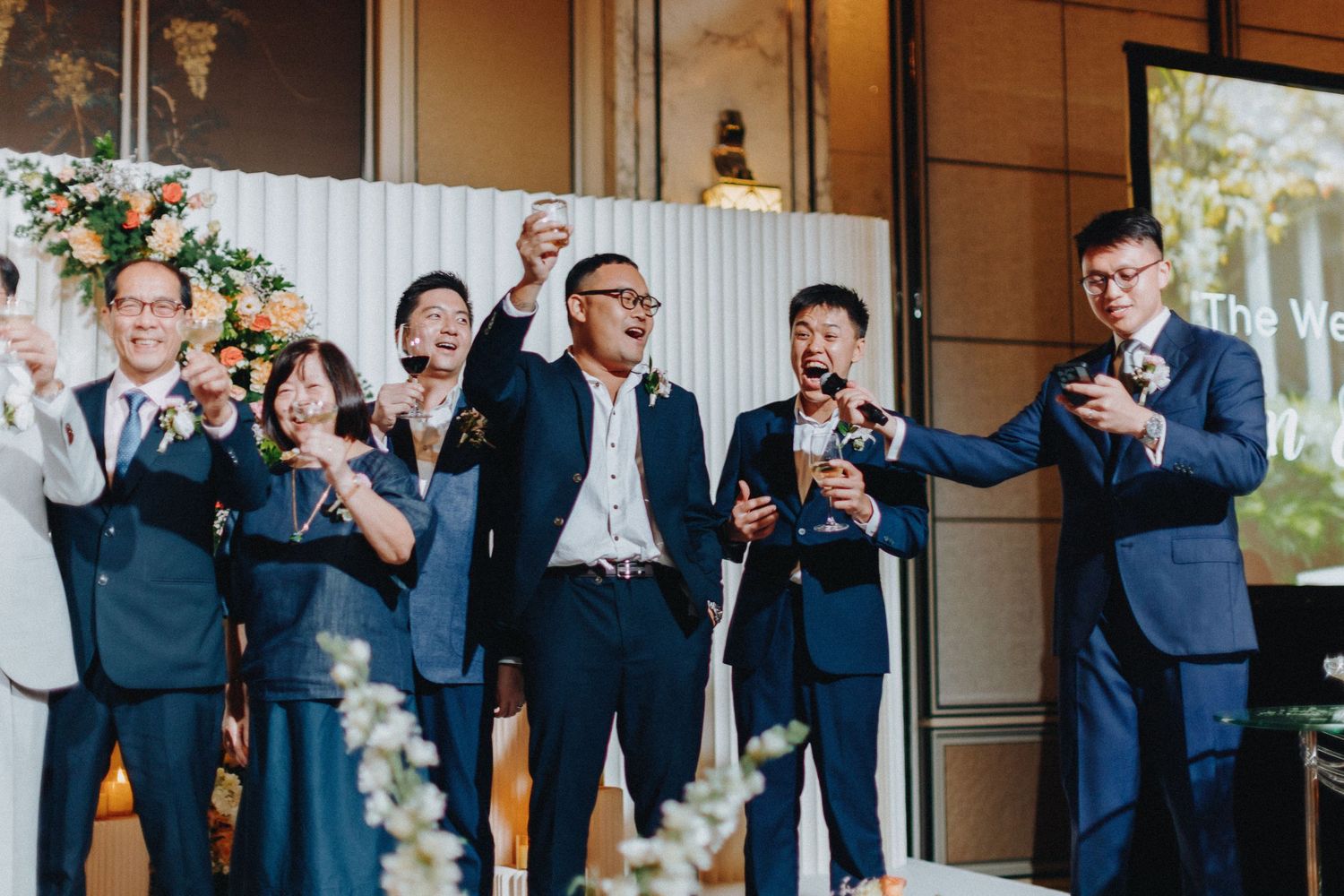 Wedding guests applaud during ceremony in an elegant venue with floral decorations.