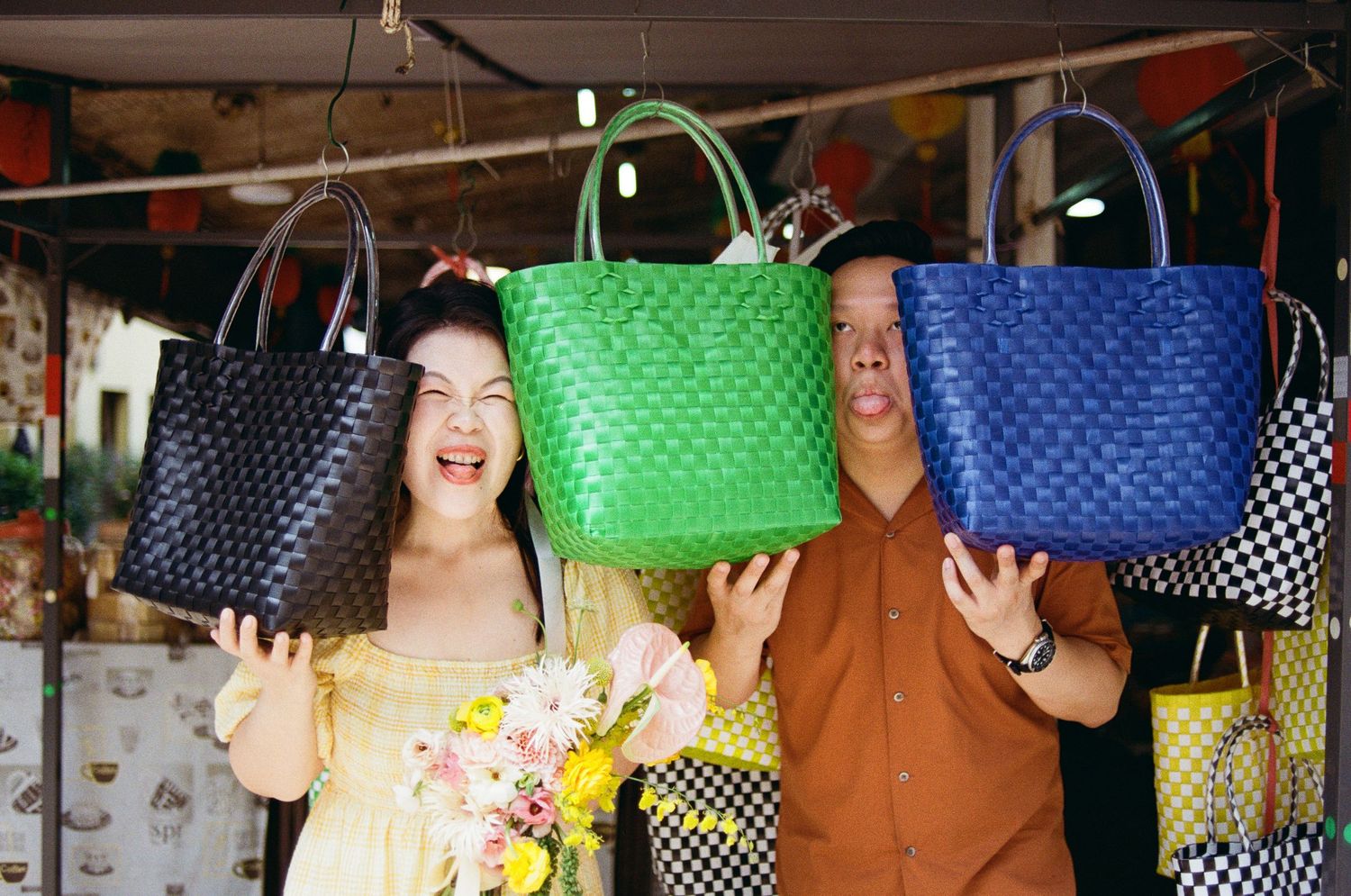 Three colorful woven handbags in navy, green, and blue being held up at a market stall.