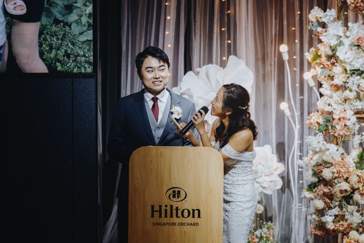 Wedding reception speech moment at a Hilton podium with decorative floral arrangements.