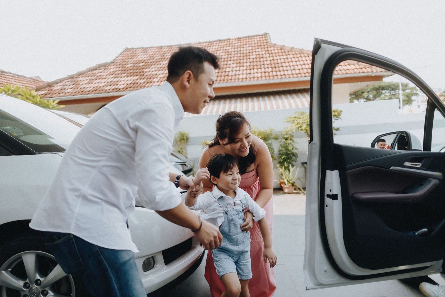 People getting into a car together outside a house with terracotta roof tiles on a bright day.