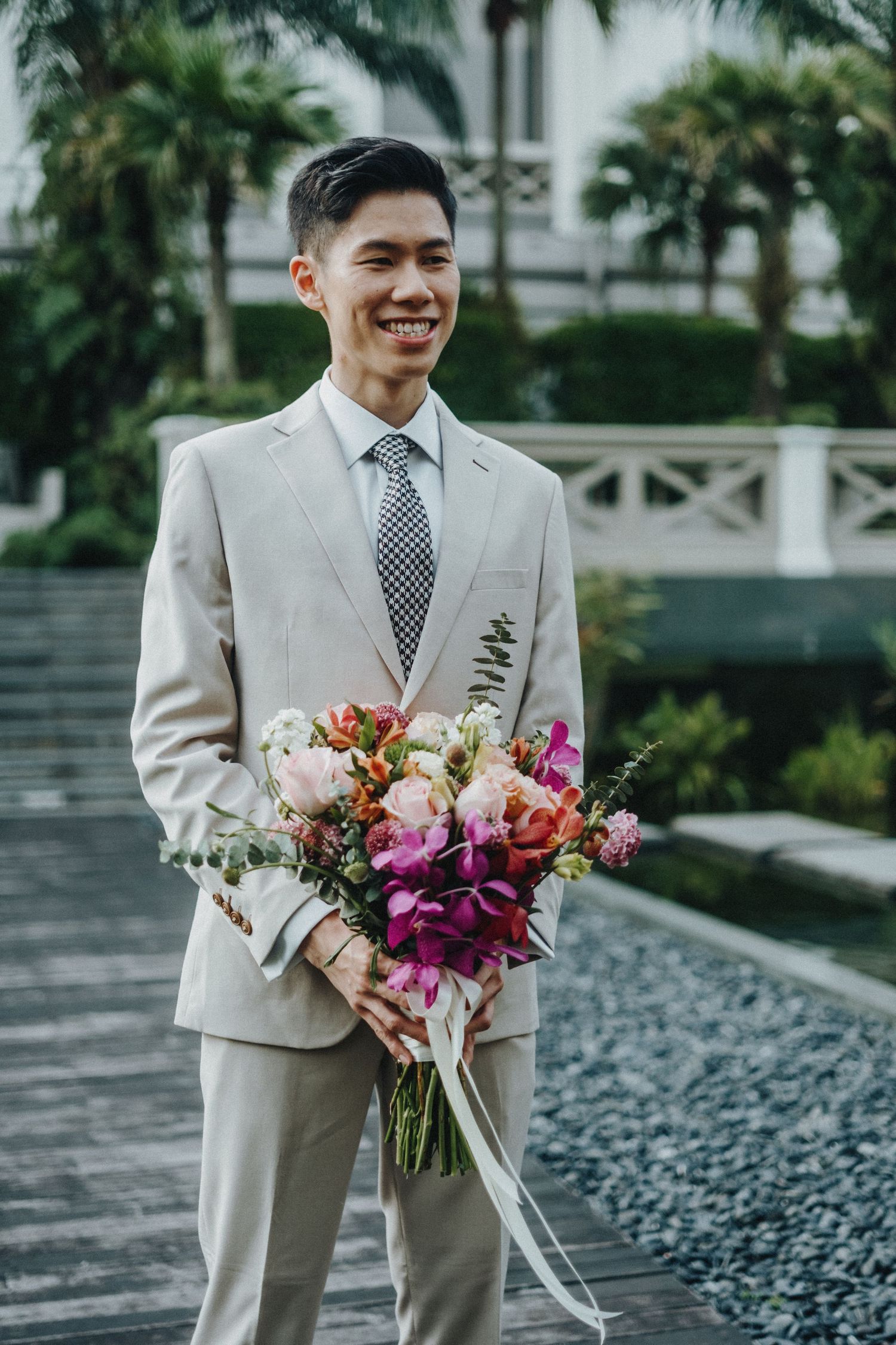 Person in light beige suit holding a vibrant bouquet with purple and pink flowers.