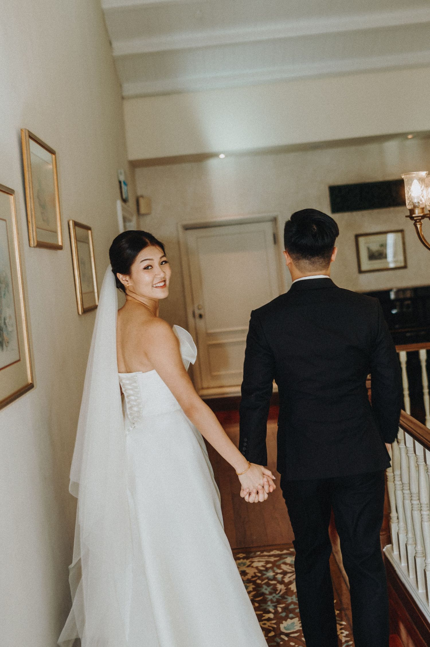 Bride and groom walk together through a hallway decorated with framed artwork.