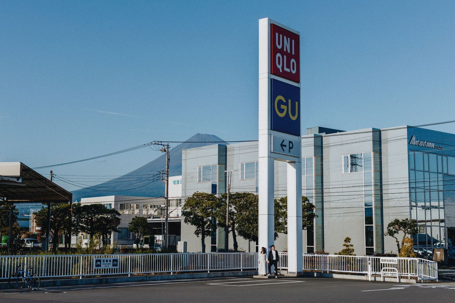 Modern retail buildings and mall entrances with glass facades and signage under a blue sky.