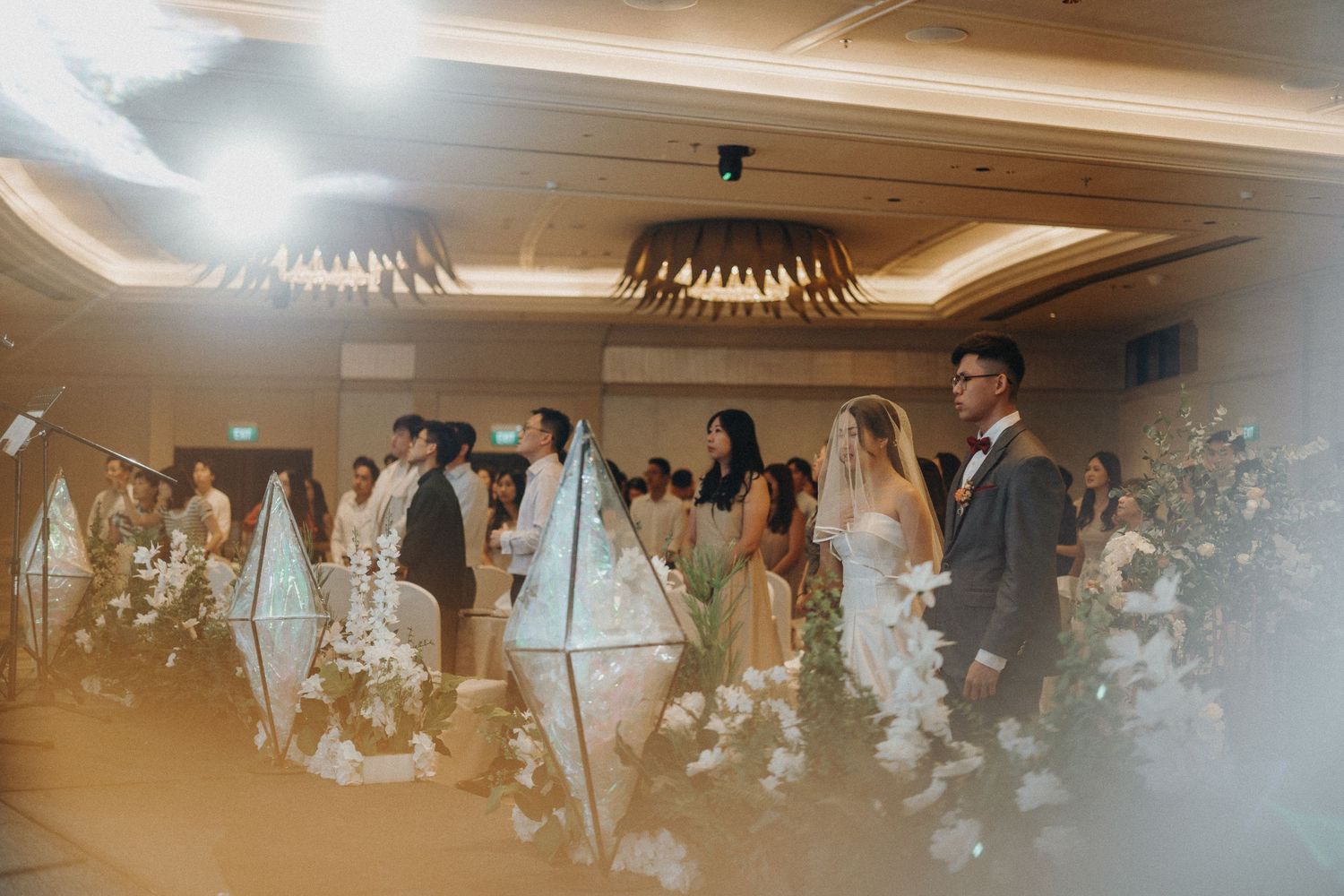 Wedding ceremony in a hotel ballroom with guests standing for an emotional moment.