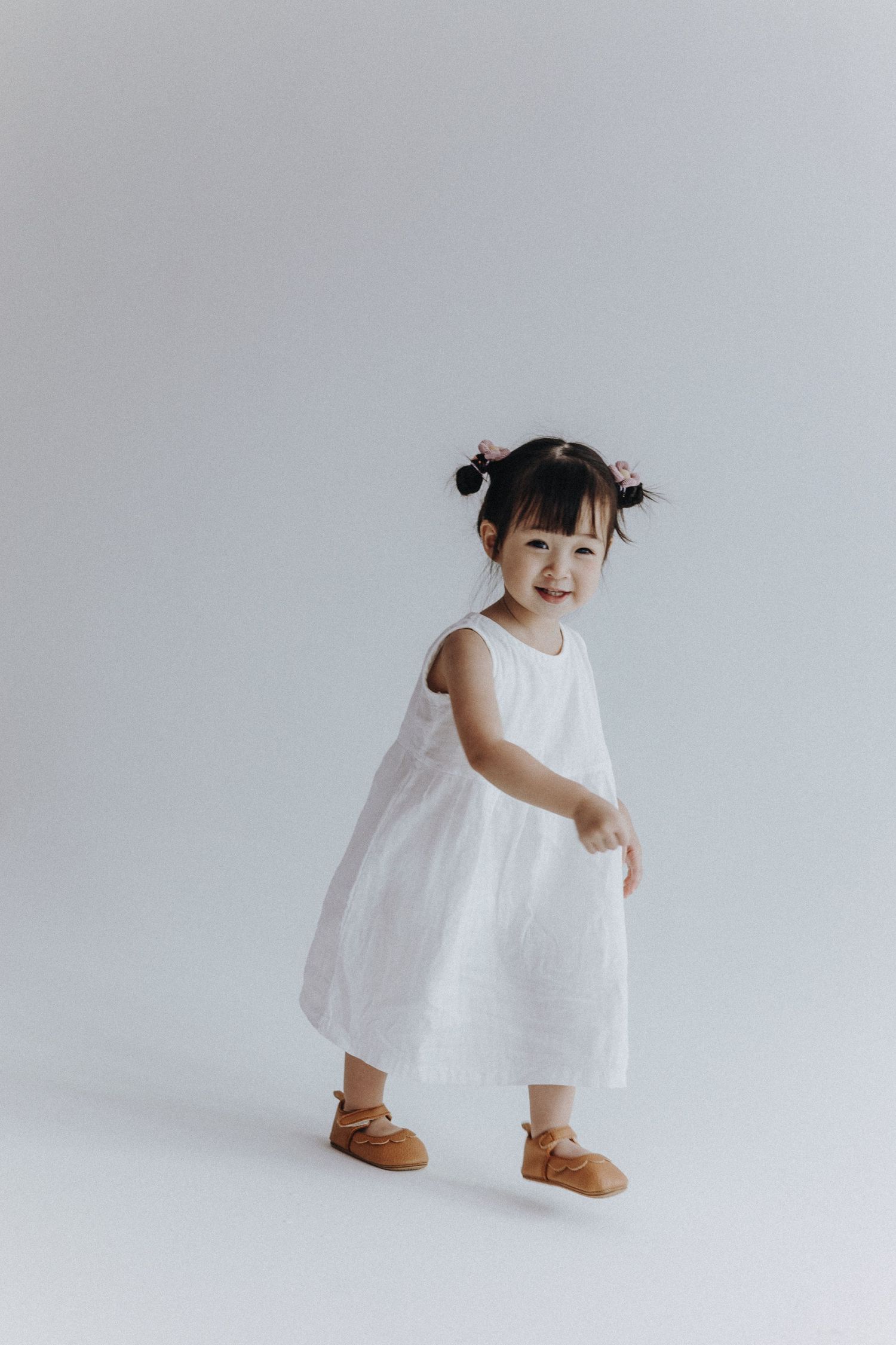 A small child in a white dress playing against a minimalist white background.