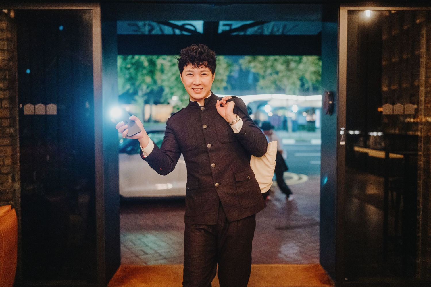 Formal suited figure poses joyfully in an elegant interior doorway setting.