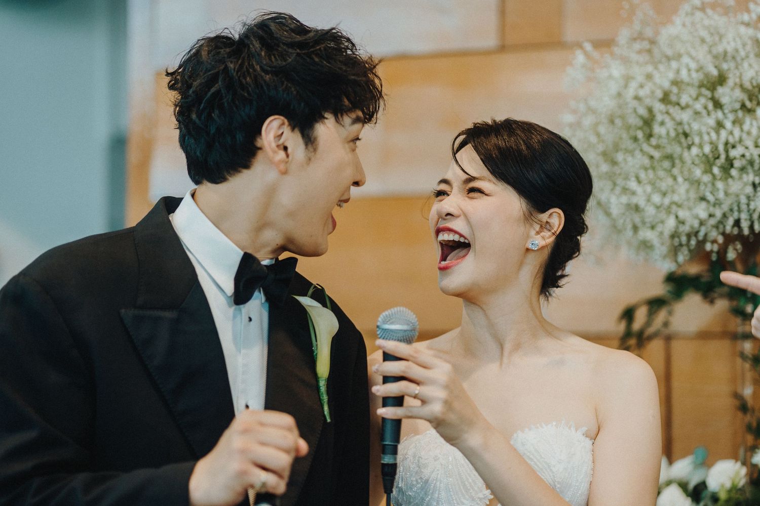 Couple sharing joyful moment with microphones during wedding celebration.
