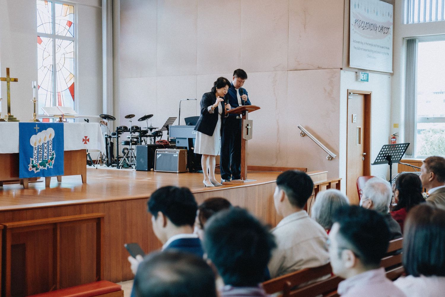 Two speakers presenting at a church podium during a religious service with seated congregation.