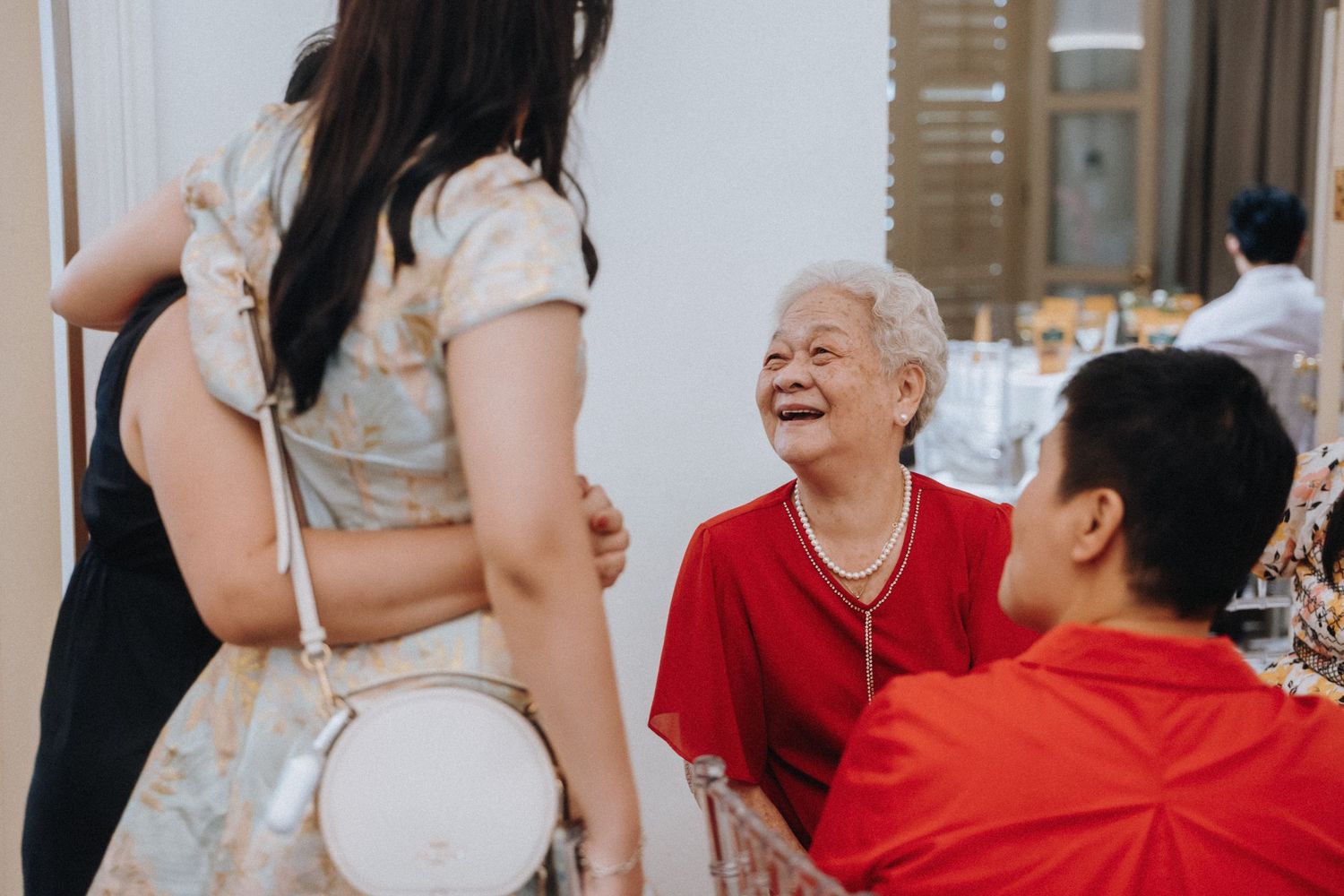 Elderly woman in red dress laughs warmly with wedding guests at reception.