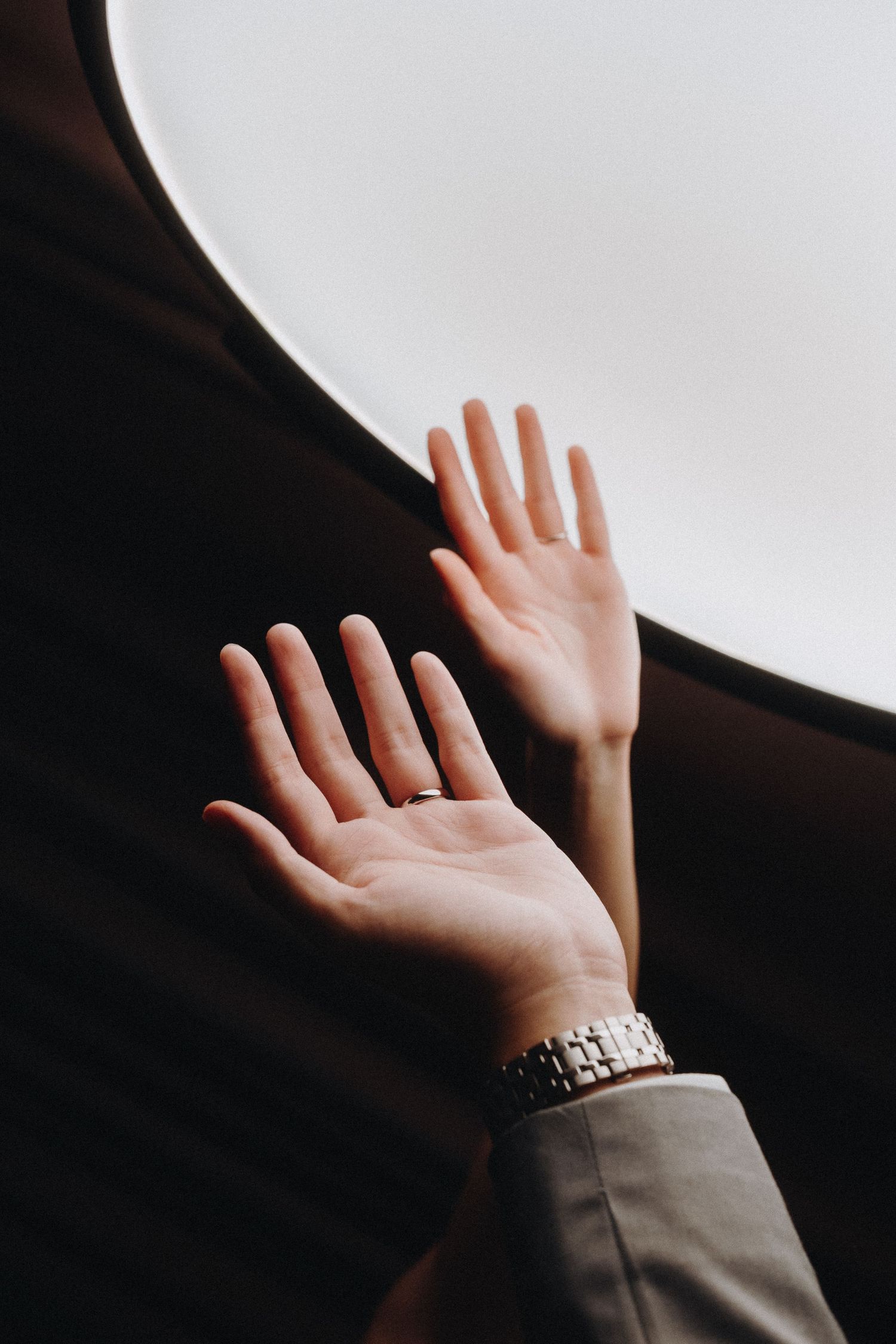 Two hands reach upward against a white background wearing a silver watch.