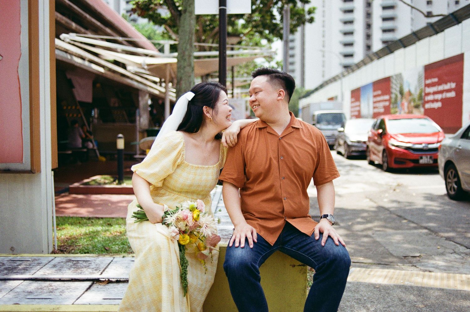 A couple shares a romantic moment sitting outdoors on a city street with a bouquet of flowers.