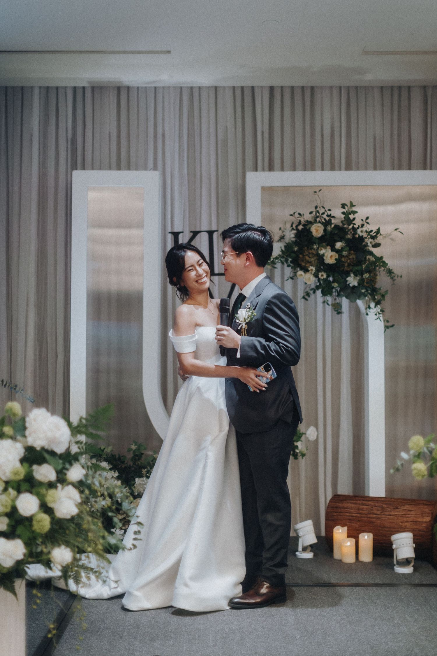 Newlyweds share an intimate moment in front of floral decor and white curtains at their wedding reception.