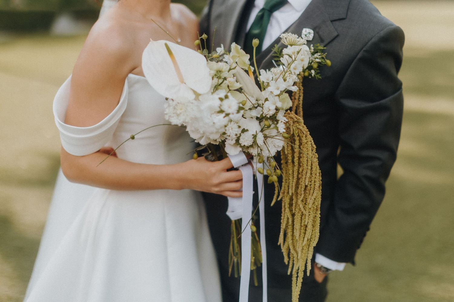 Elegant wedding bouquet with white flowers and golden tassels held at outdoor ceremony.