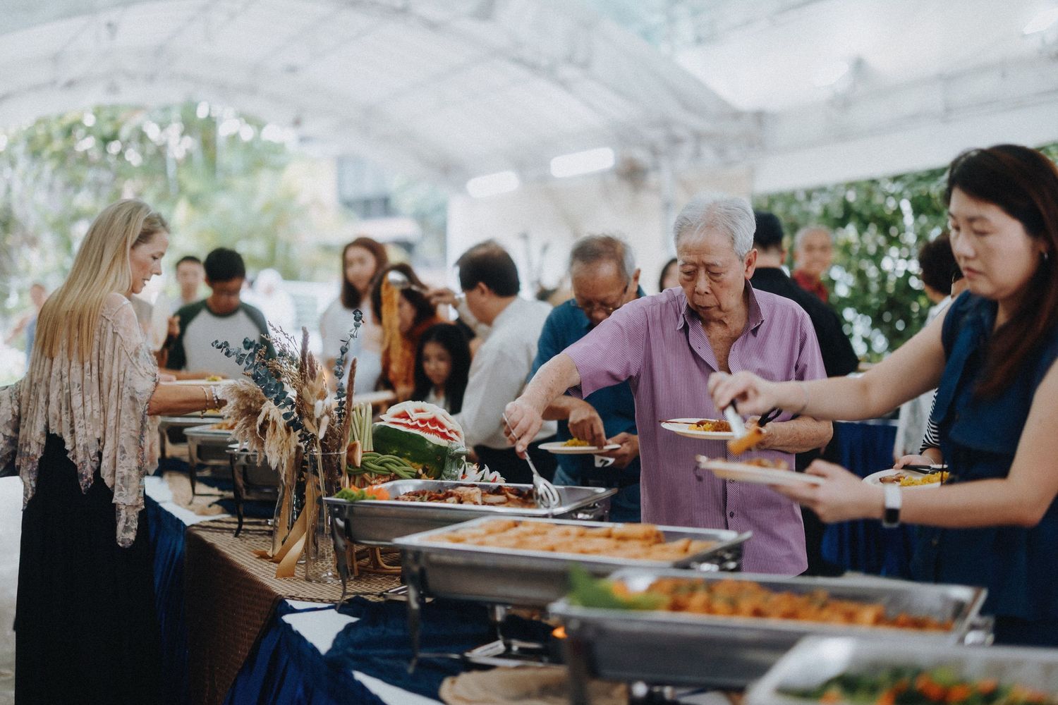 People serve themselves at a buffet line with multiple chafing dishes of food.