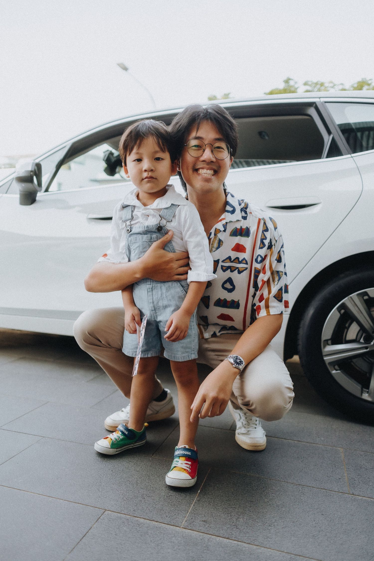 Two people sit together in a bright indoor space with parked cars visible in the background.