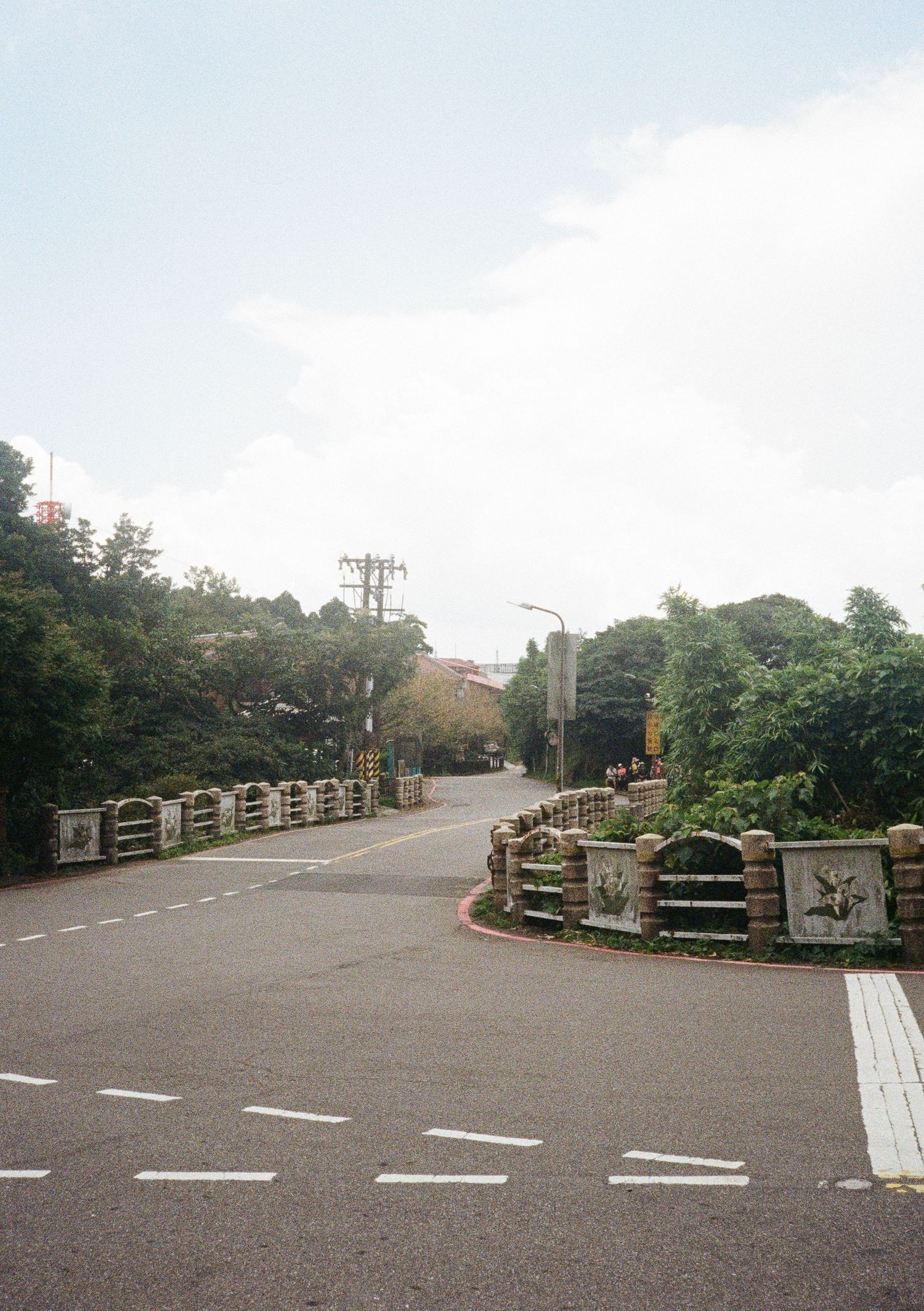Curved road with stone barriers and trees leading into a misty suburban area.