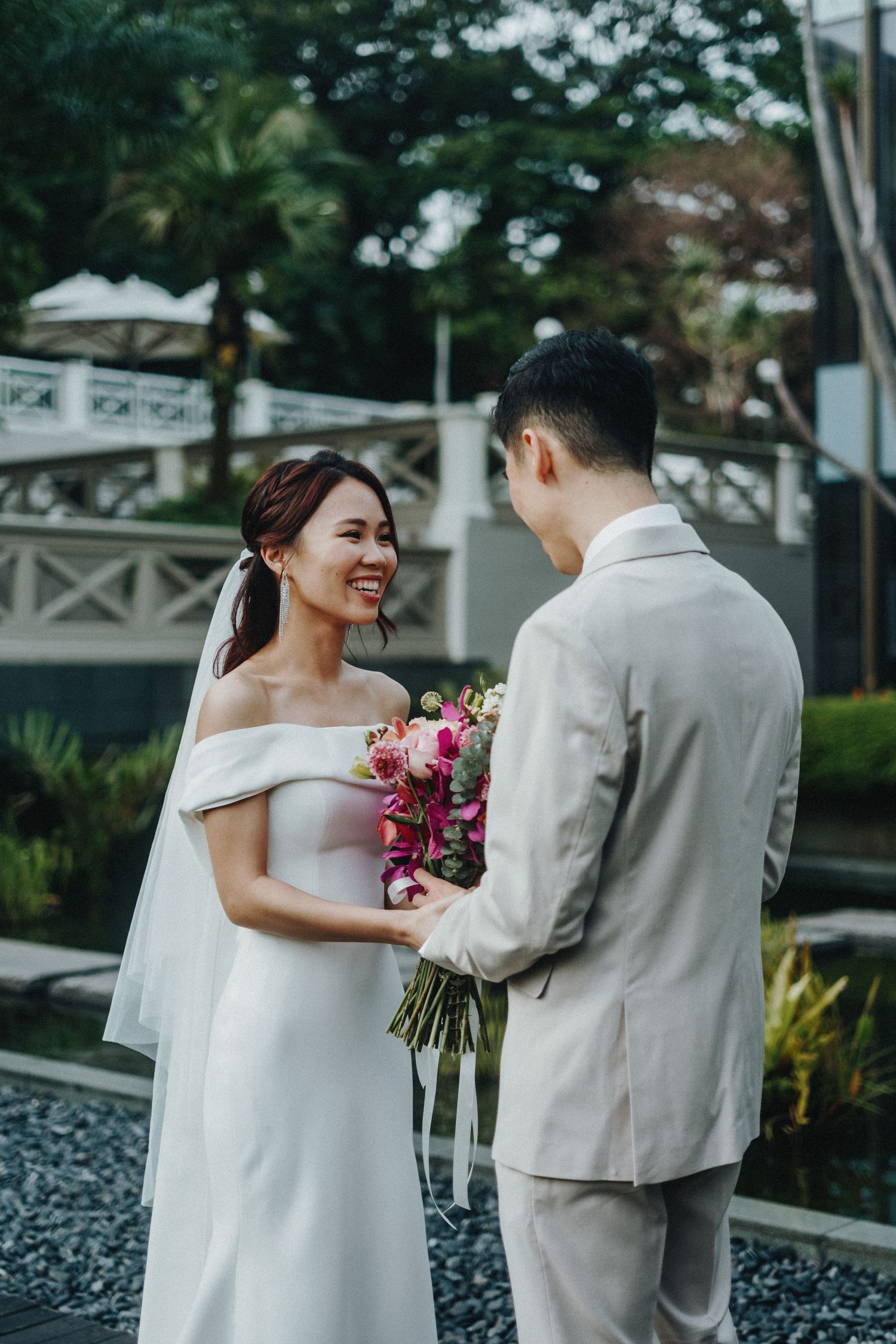 A couple in wedding attire shares intimate moments outdoors with pink bouquet and garden setting.