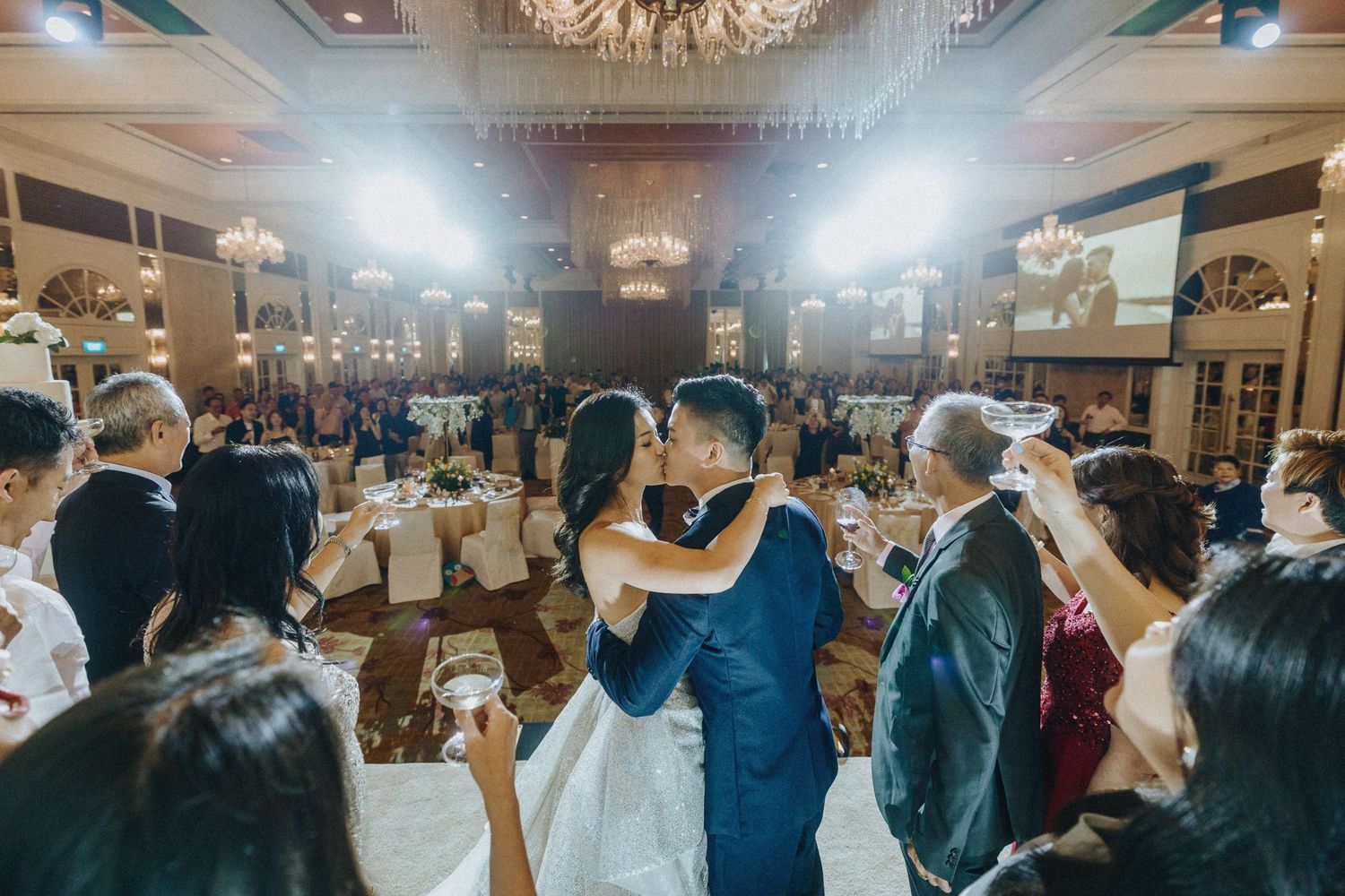 Wedding reception ballroom filled with guests dancing under crystal chandeliers.