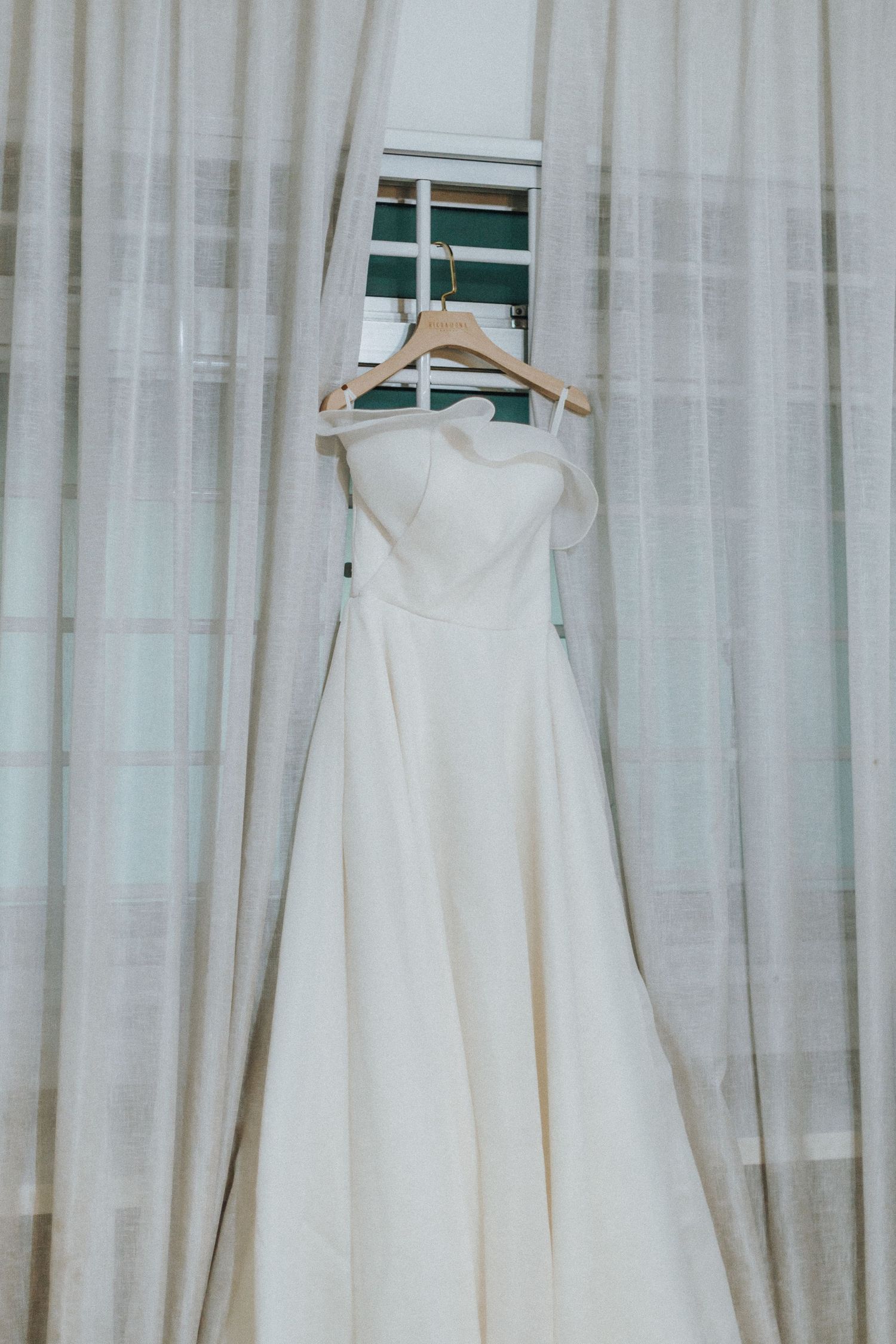 Several white wedding dresses hanging on display against a white curtained wall.