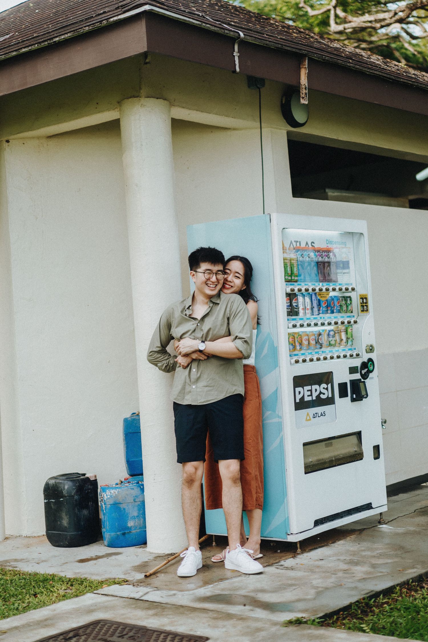 A couple embraces beside a retro-style Pepsi vending machine on a covered patio with white pillars.