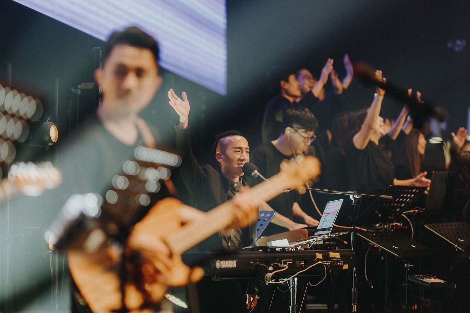 Musicians perform with guitars and electronic equipment on stage during a live concert.