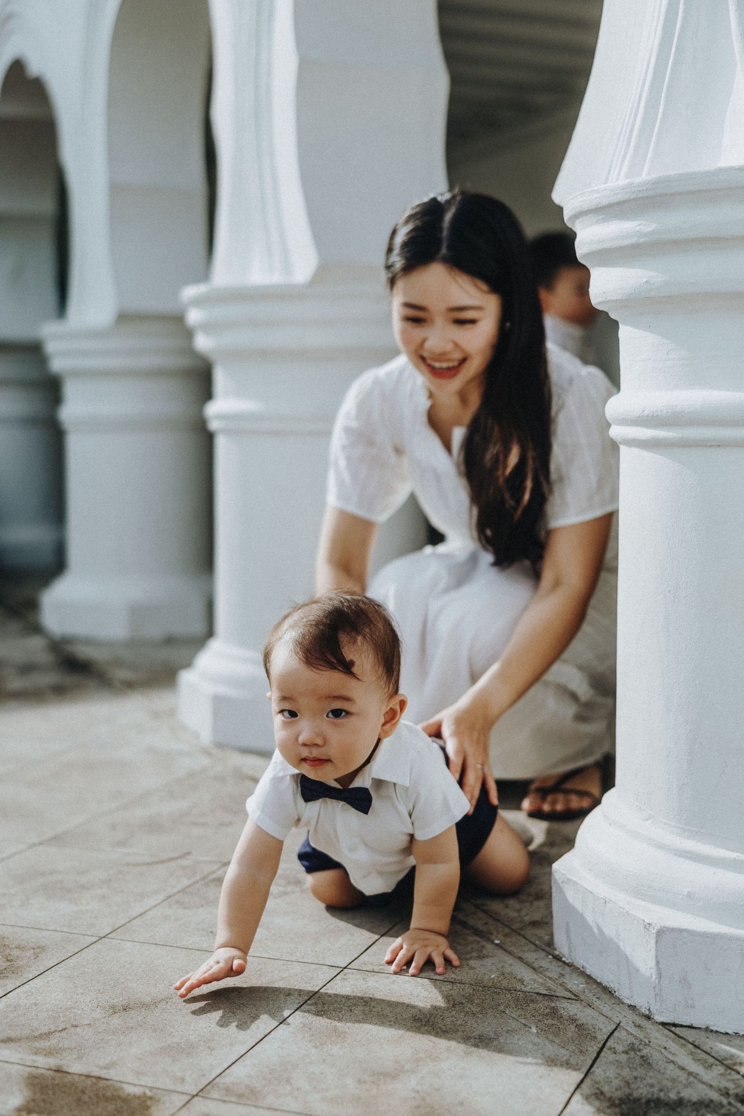 Joyful moment captured in white colonial architecture as toddler crawls on tiled floor.