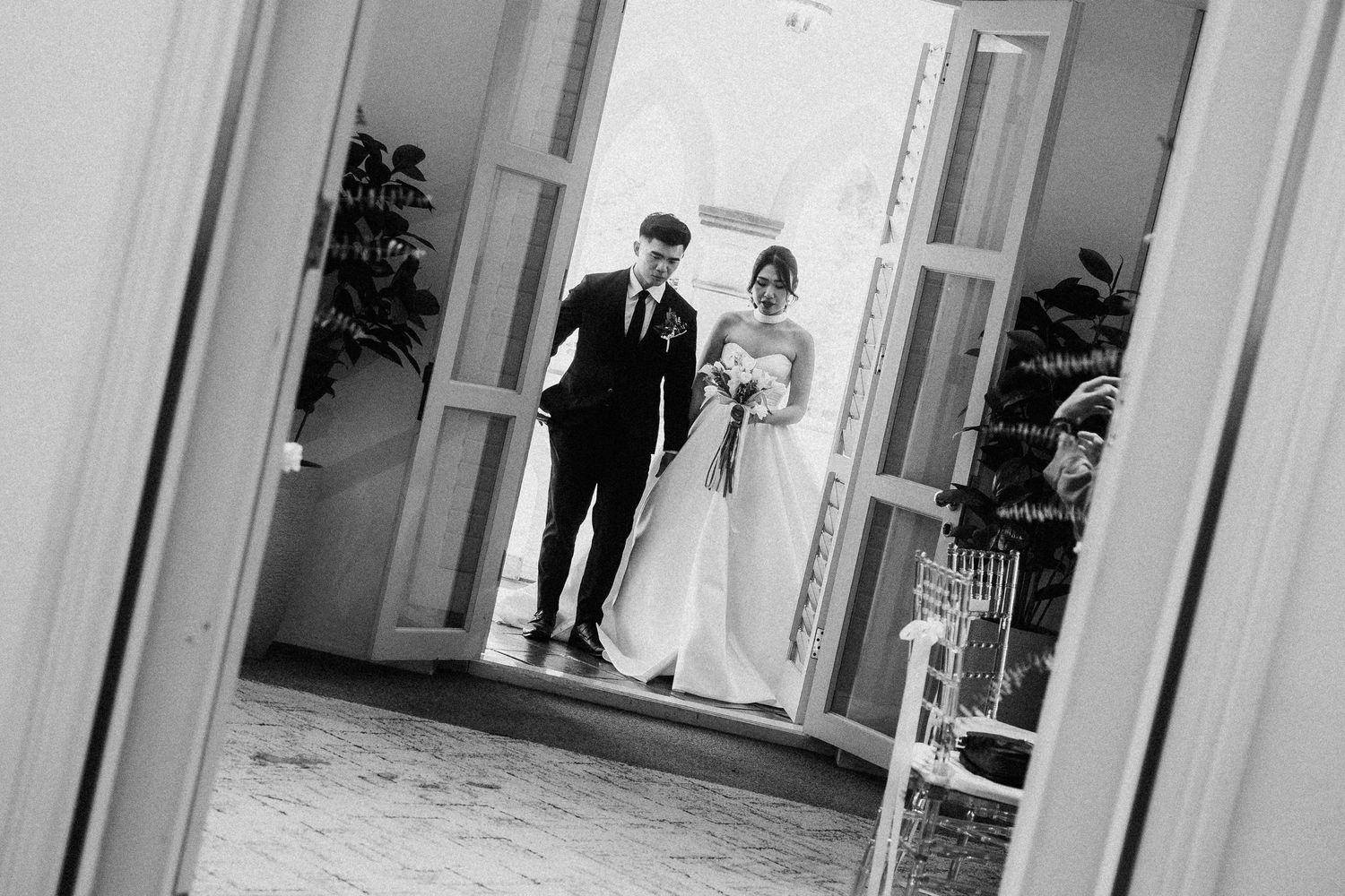Bride and groom make a grand entrance through elegant double doors in a classic black and white wedding photo.