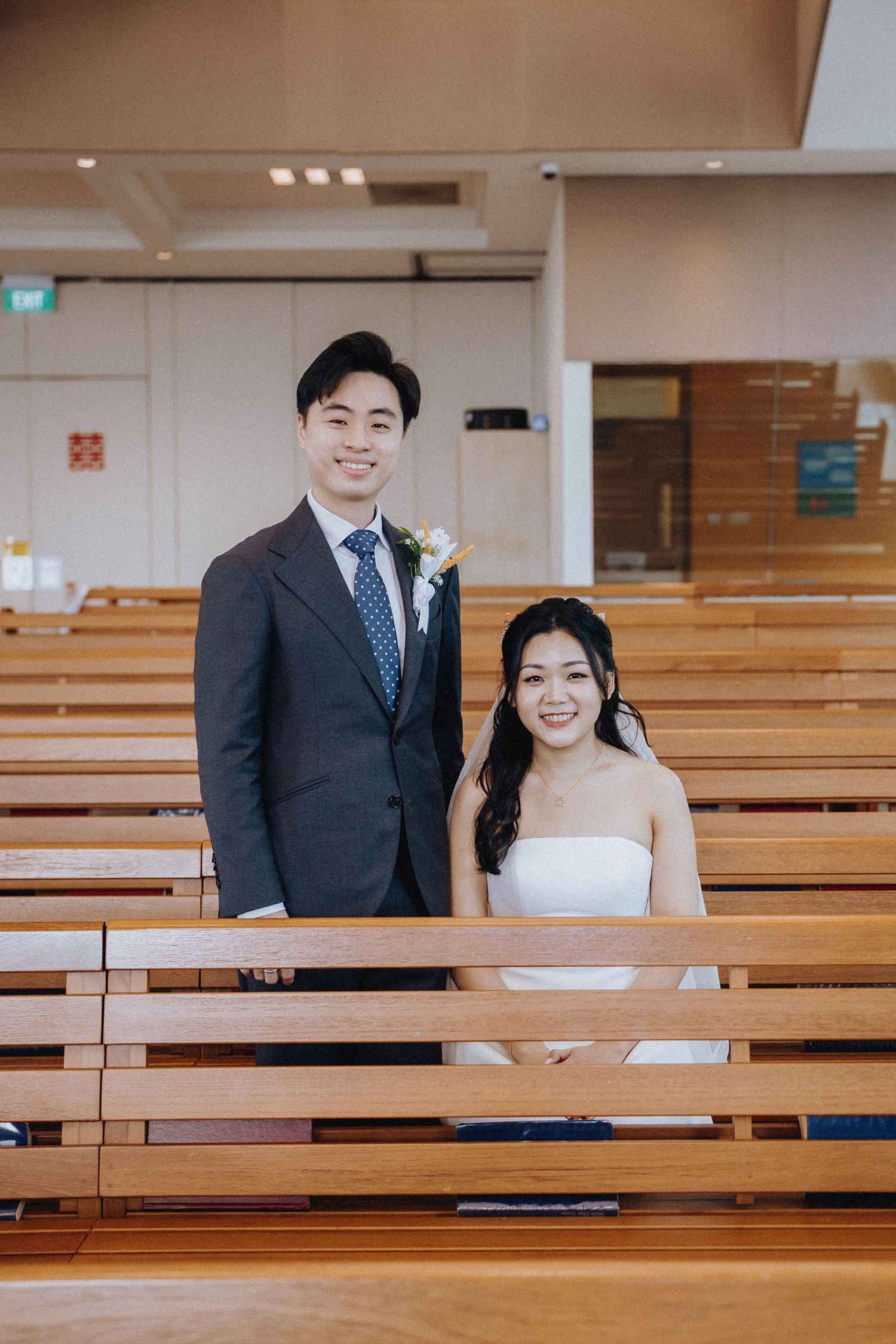Smiling bride and groom posing between wooden church pews on their wedding day.