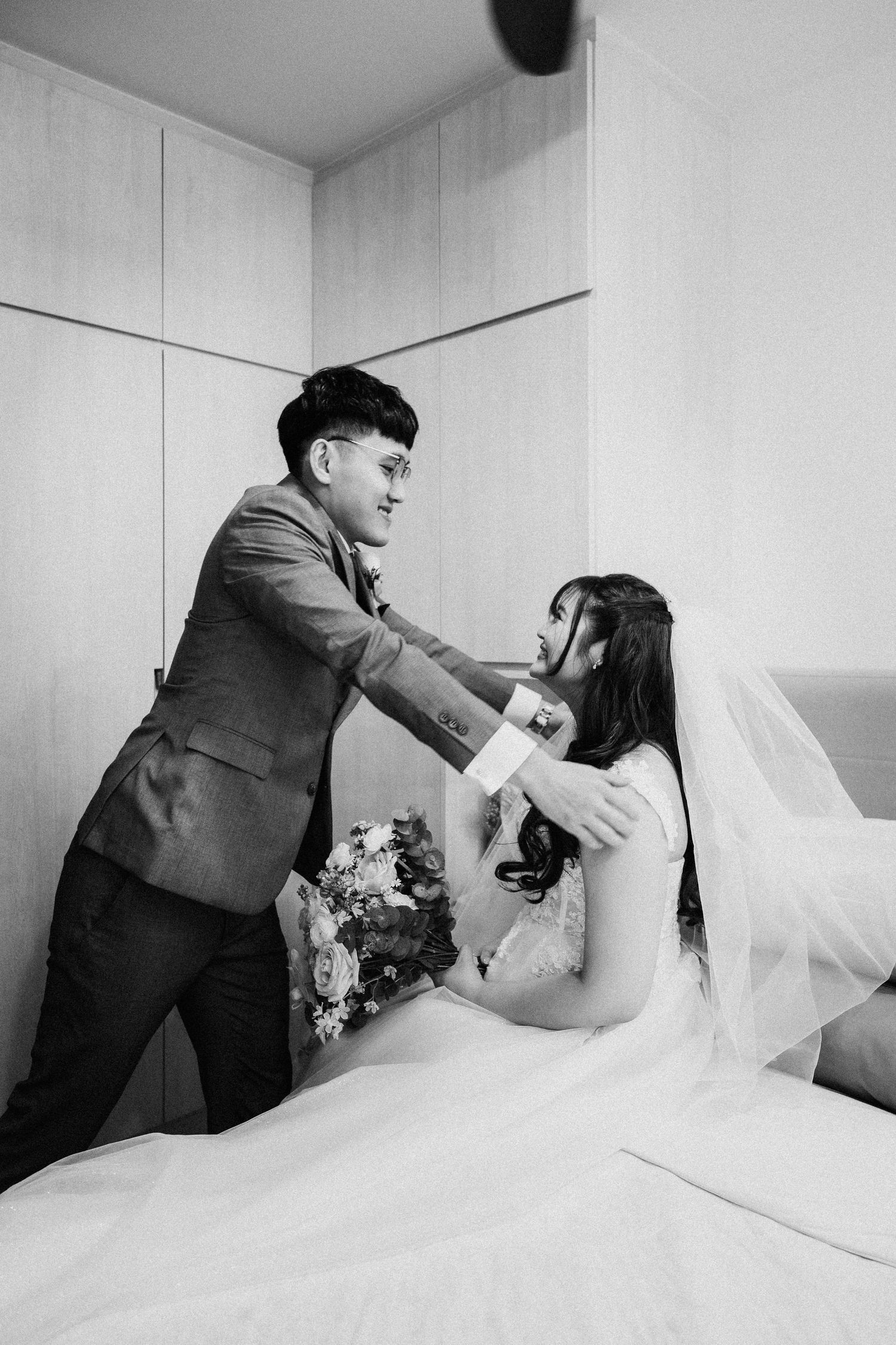 A candid black and white moment between a bride in her wedding dress and groom in a suit during preparation.