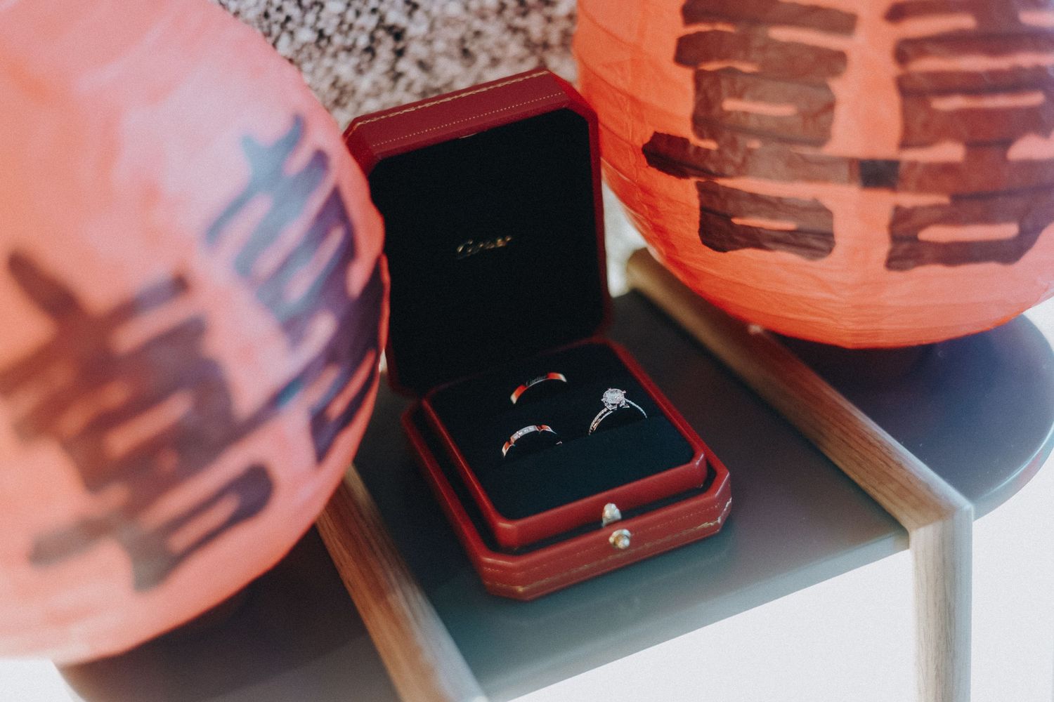 Wedding rings rest in a red velvet box beside pink paper lanterns with Chinese characters.