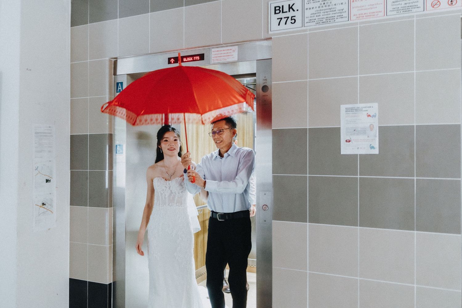 Wedding couple with red umbrella walking through modern building corridor.