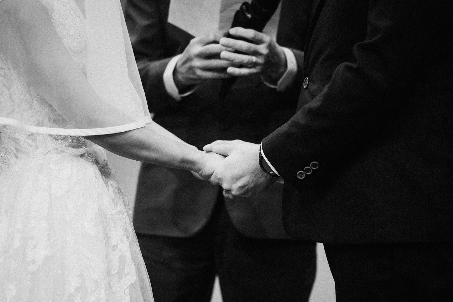 Black and white detail shot of wedding ceremony participants standing in formal attire.