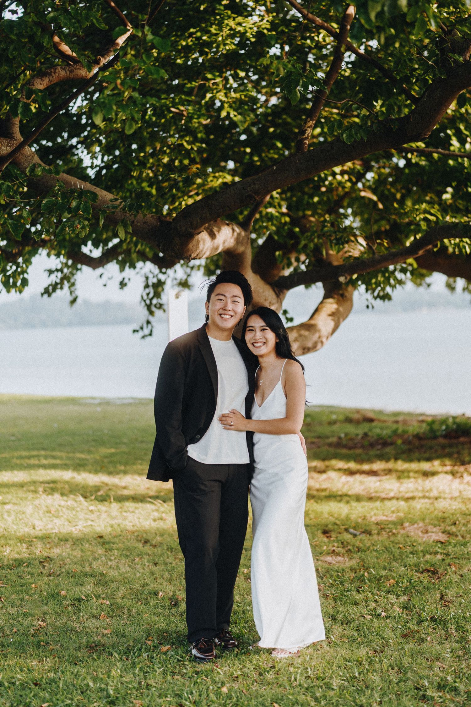 Happy couple sharing intimate moments under a large tree by the water.