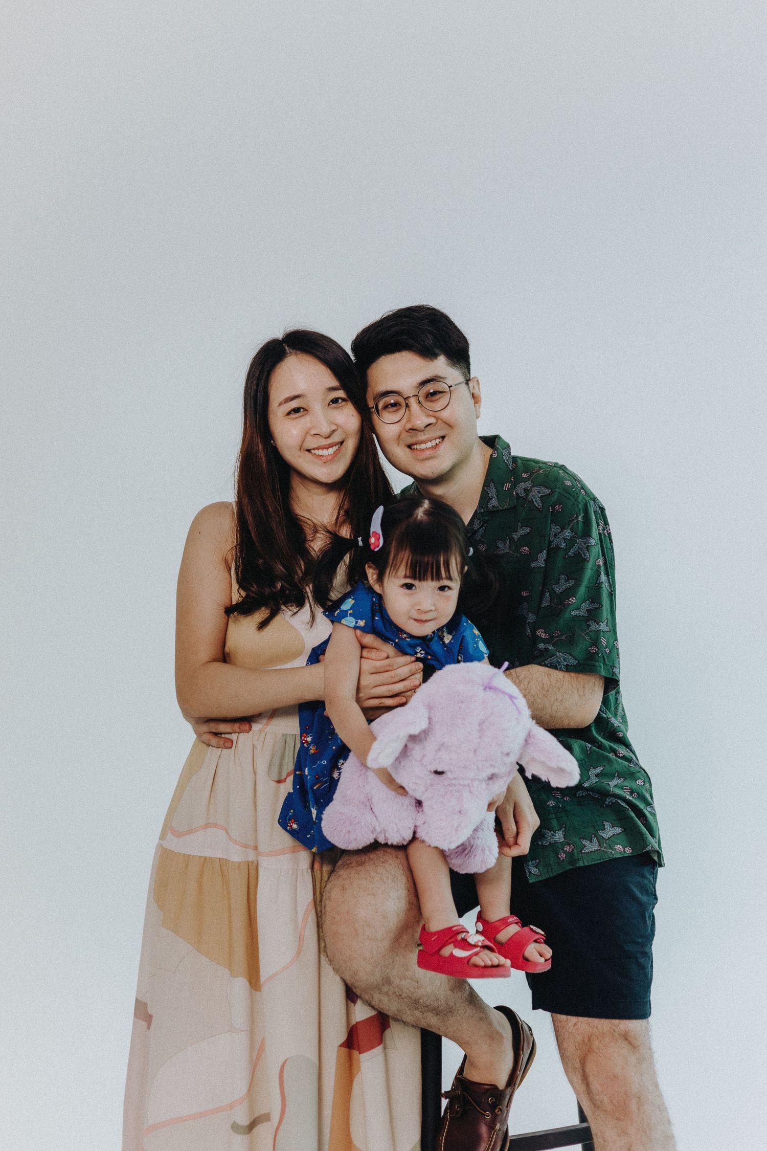 Family poses together in coordinated outfits with stuffed animal against white backdrop.