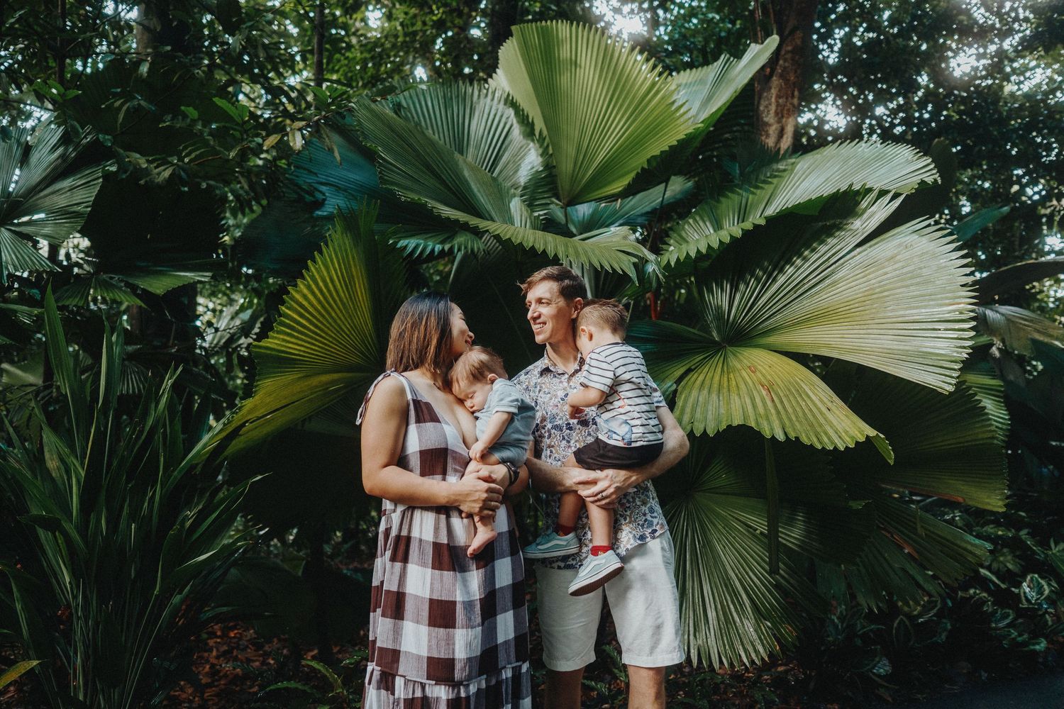 Family gathered together in front of dramatic fan palm leaves in tropical garden setting.
