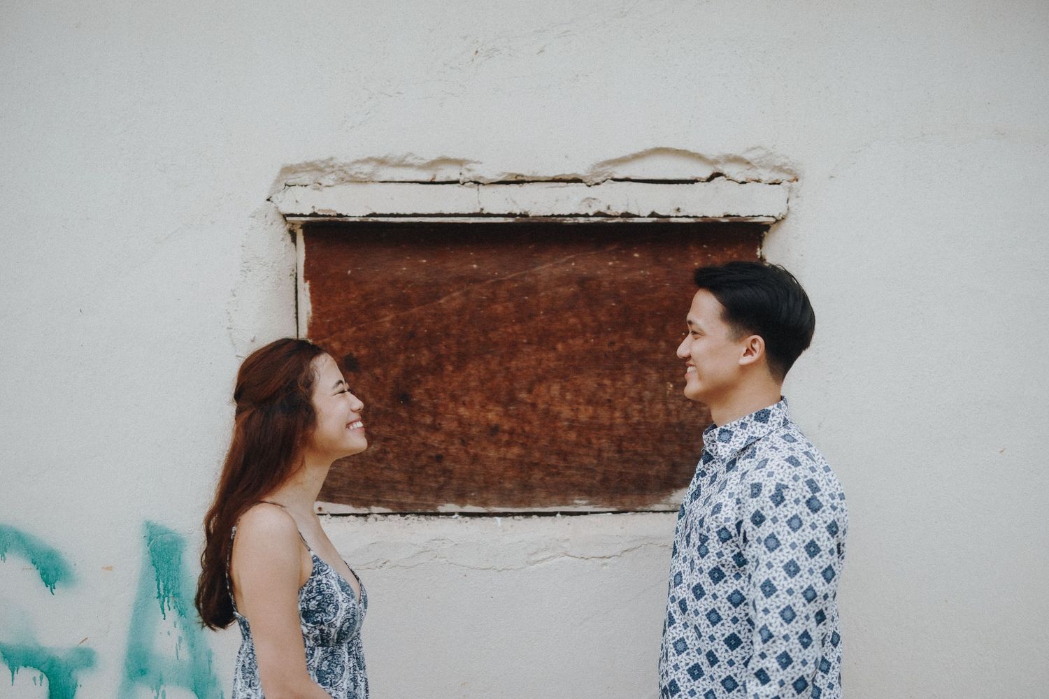 A couple in coordinated outfits share a playful moment against a rustic wall background.