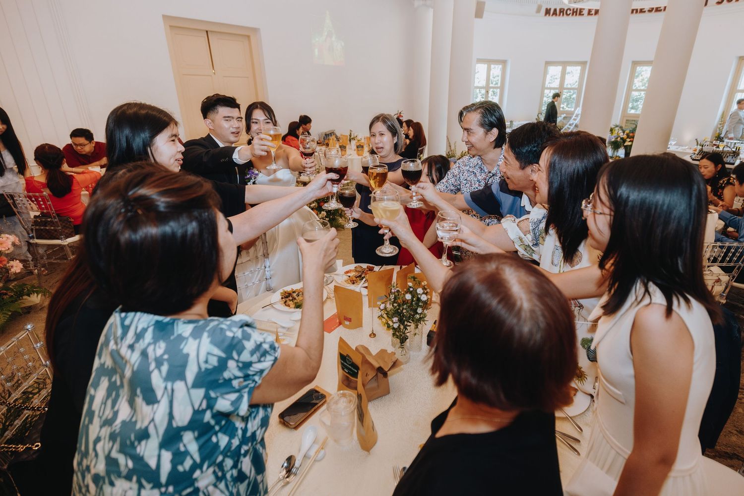 Wedding guests raise glasses in a celebratory toast at a reception dinner.