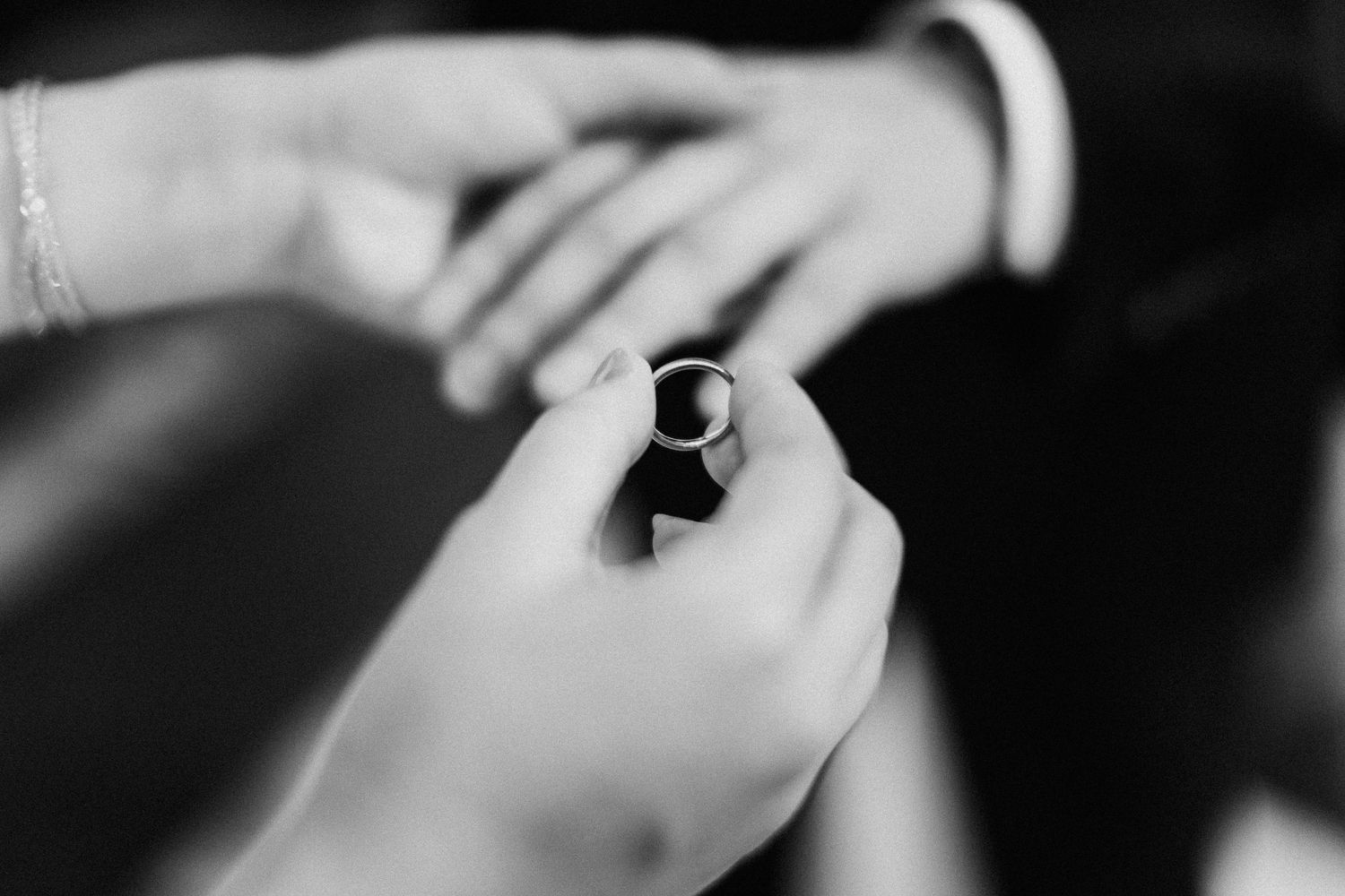 Artistic black and white close-up of wedding rings being exchanged.