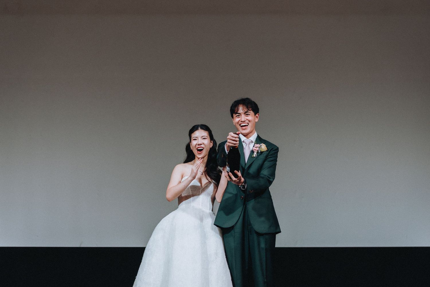 A joyful Asian bride and groom in wedding attire celebrate together on stage during their wedding reception.