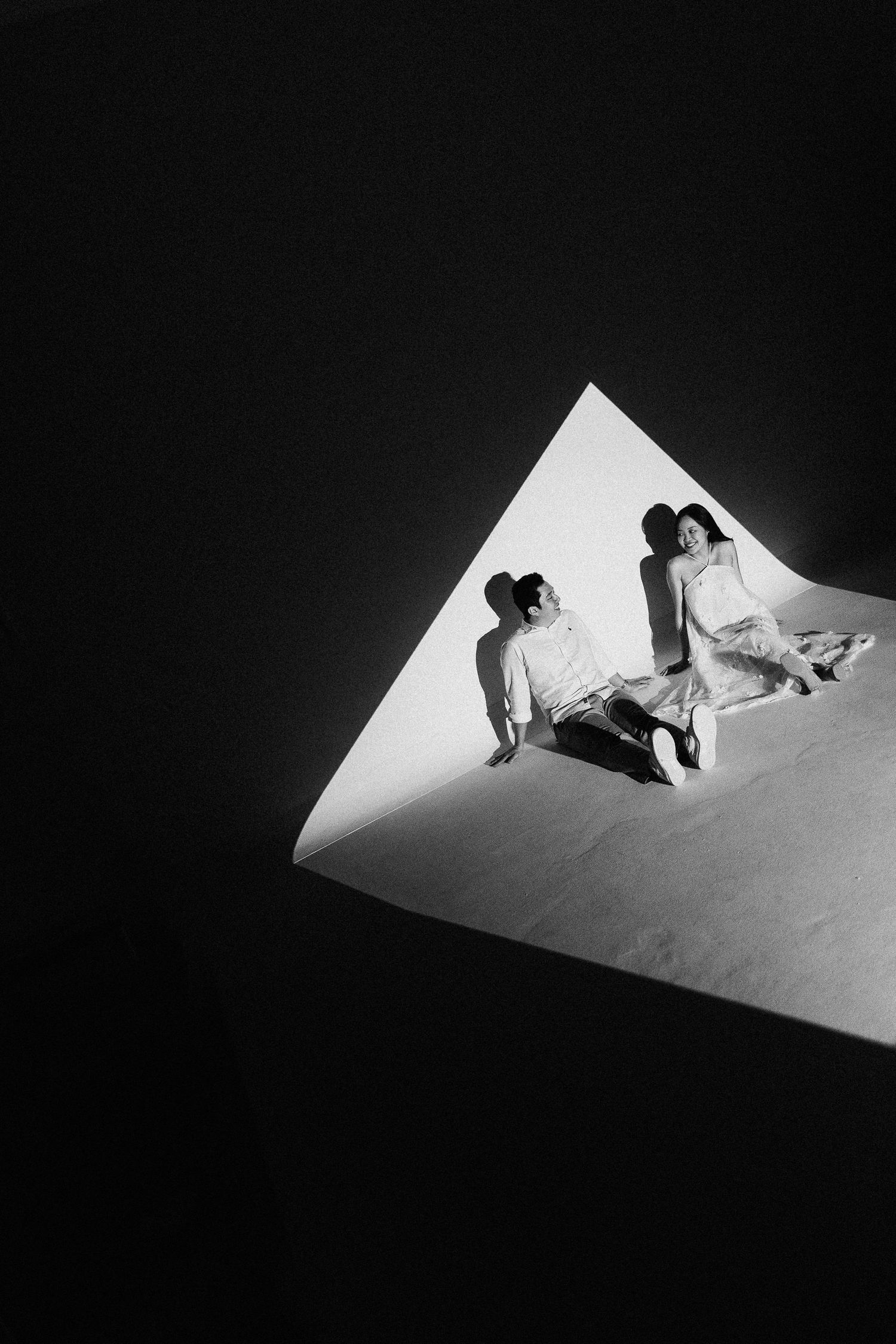Artistic black and white photo of a couple in white within a geometric triangle shape.