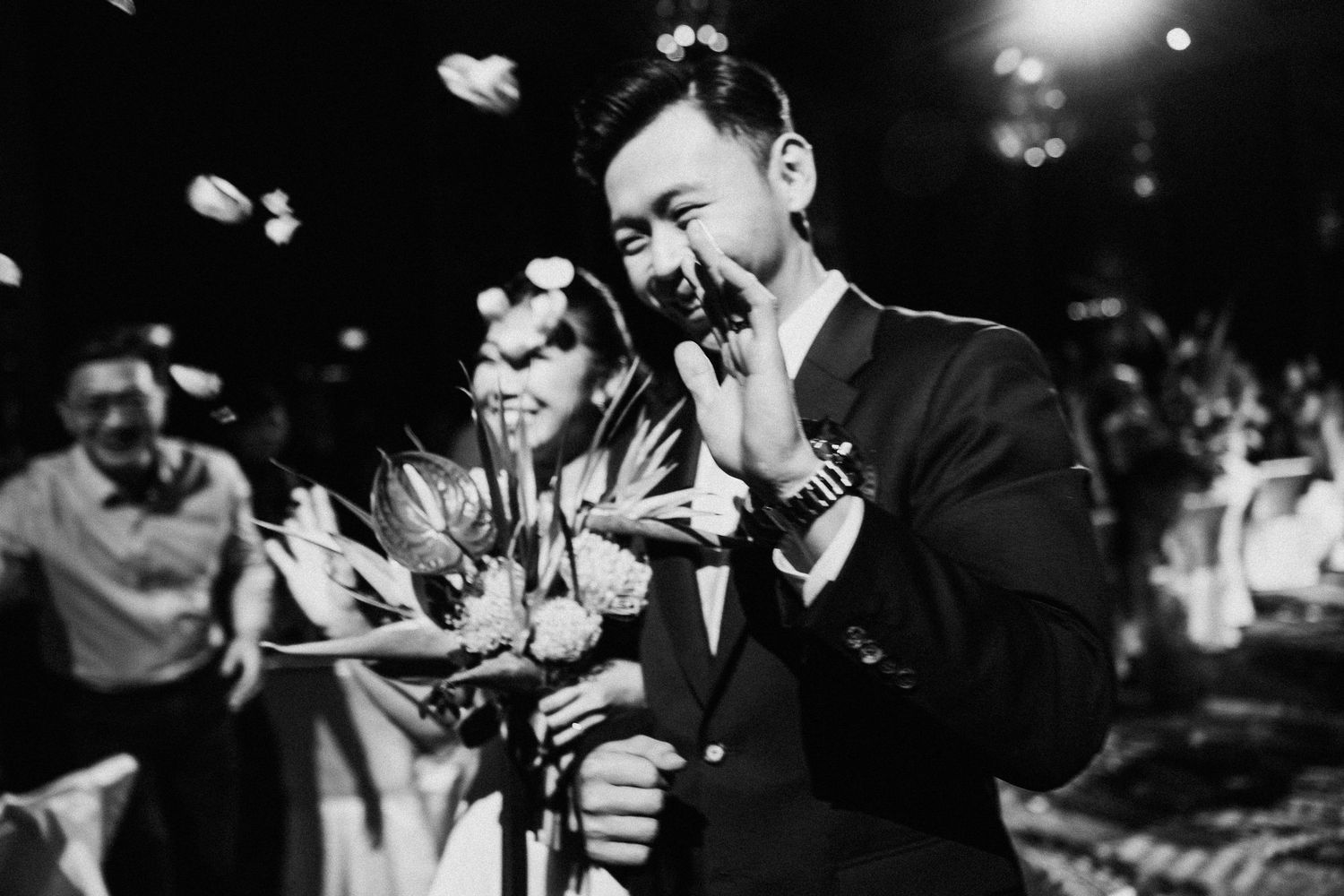 Black and white photo of wedding celebration with people throwing petals in festive atmosphere.