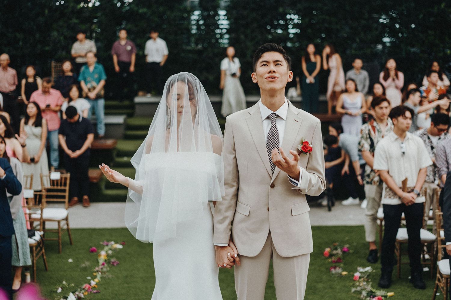 An outdoor wedding ceremony with rows of guests seated on white chairs as the couple exchanges vows.
